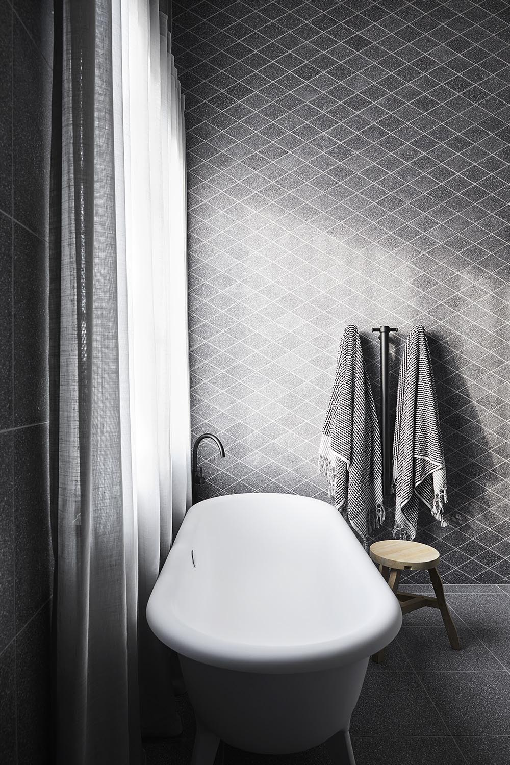 This modern main en-suite bathroom features a wall of custom diamond-cut terrazzo, a geometric shift designed to surprise and relieve the eye, while the Ottocento bath by Agape rests below the window.