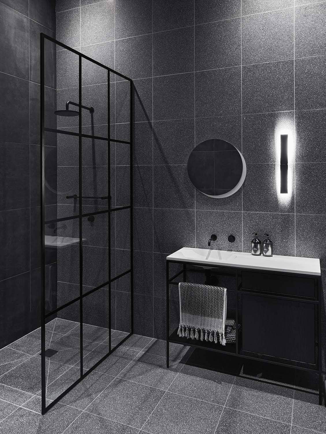 Modern grey and black bathroom with terrazzo tile covered walls, and a black framed glass shower screen.
