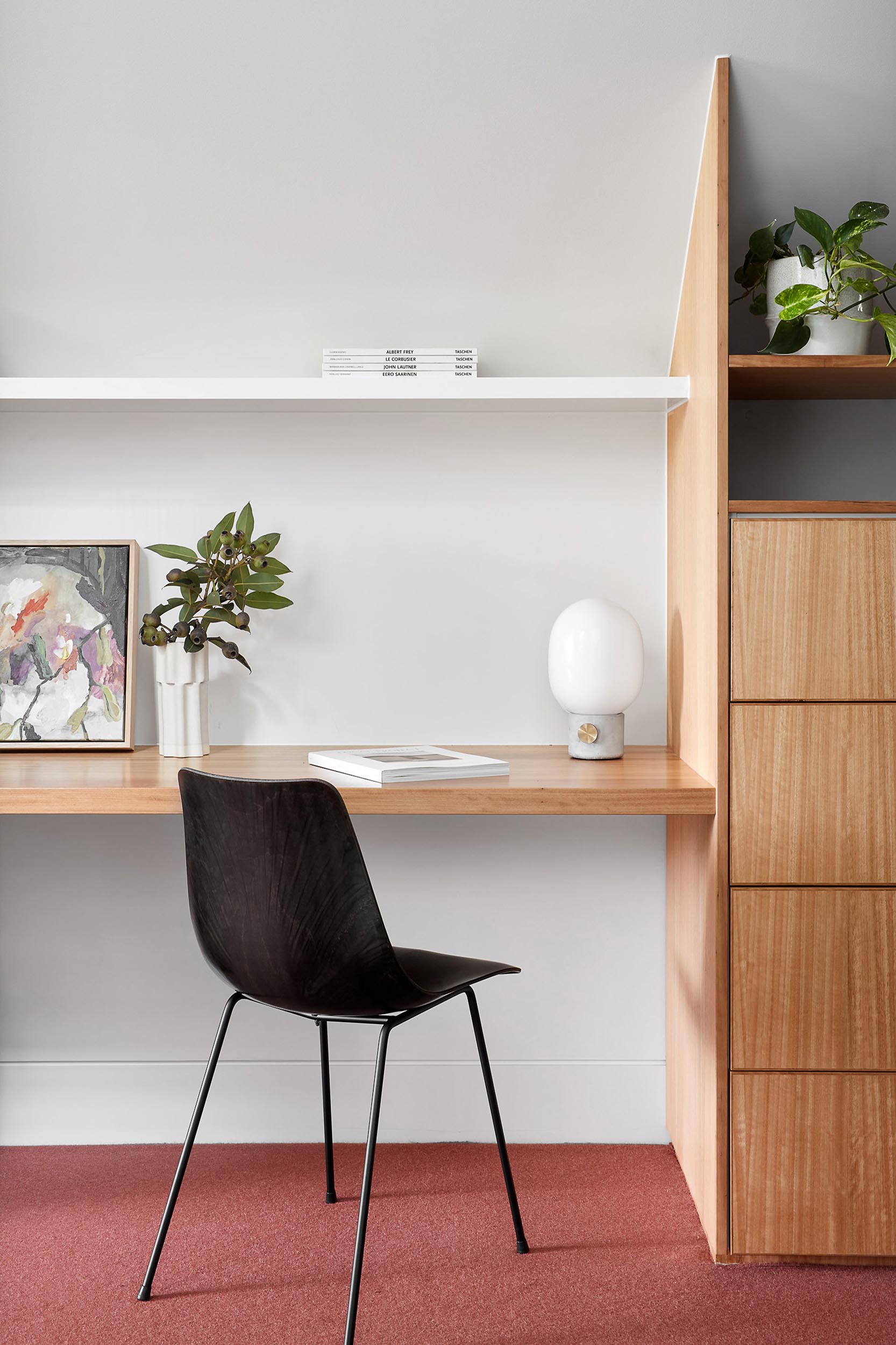 A home office includes colorful carpet, a custom designed desk and cabinets, and a white shelf.