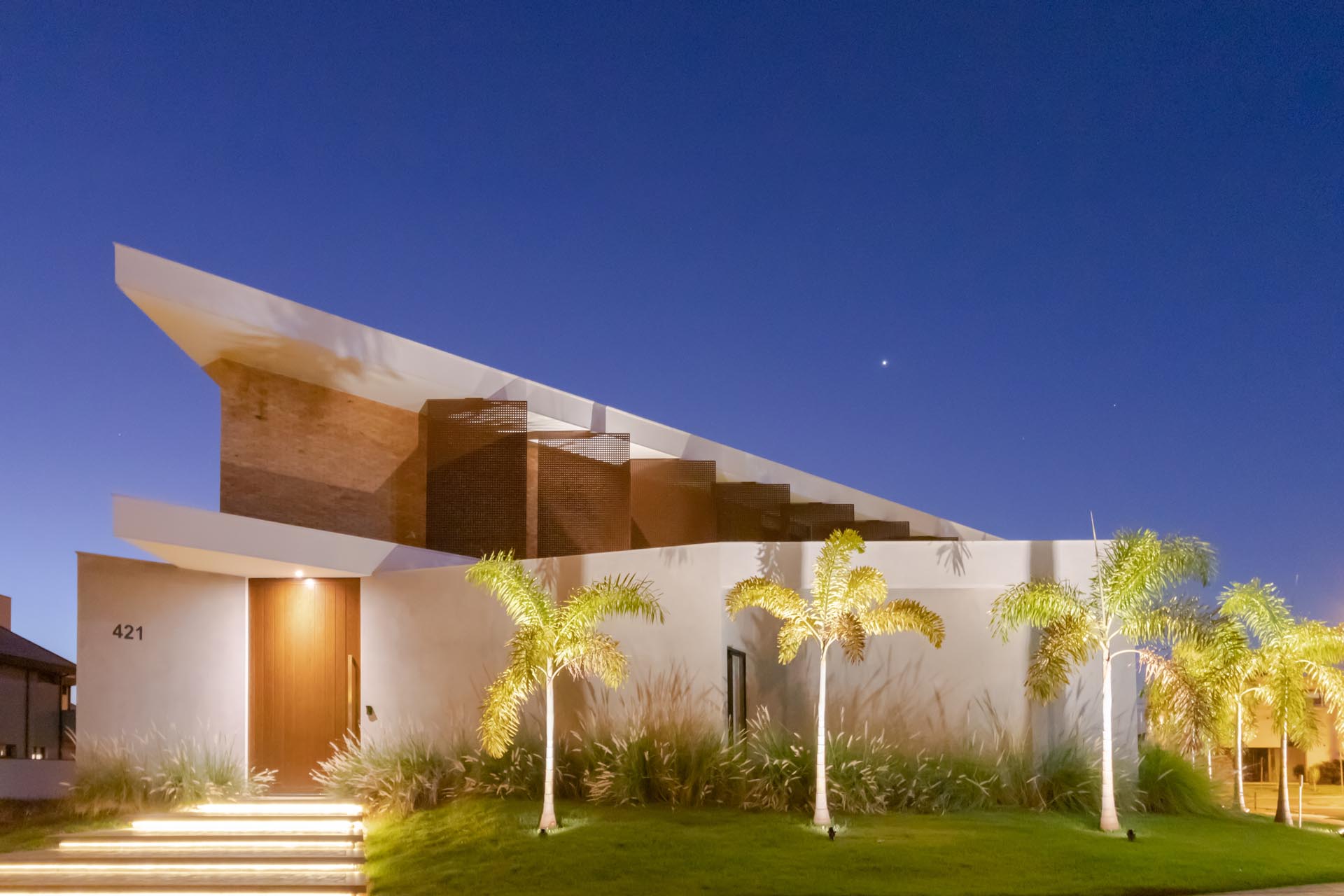 This modern home is located on an irregular corner lot, with the curb appeal showcasing steps with hidden lighting, and uplighting the palm trees.