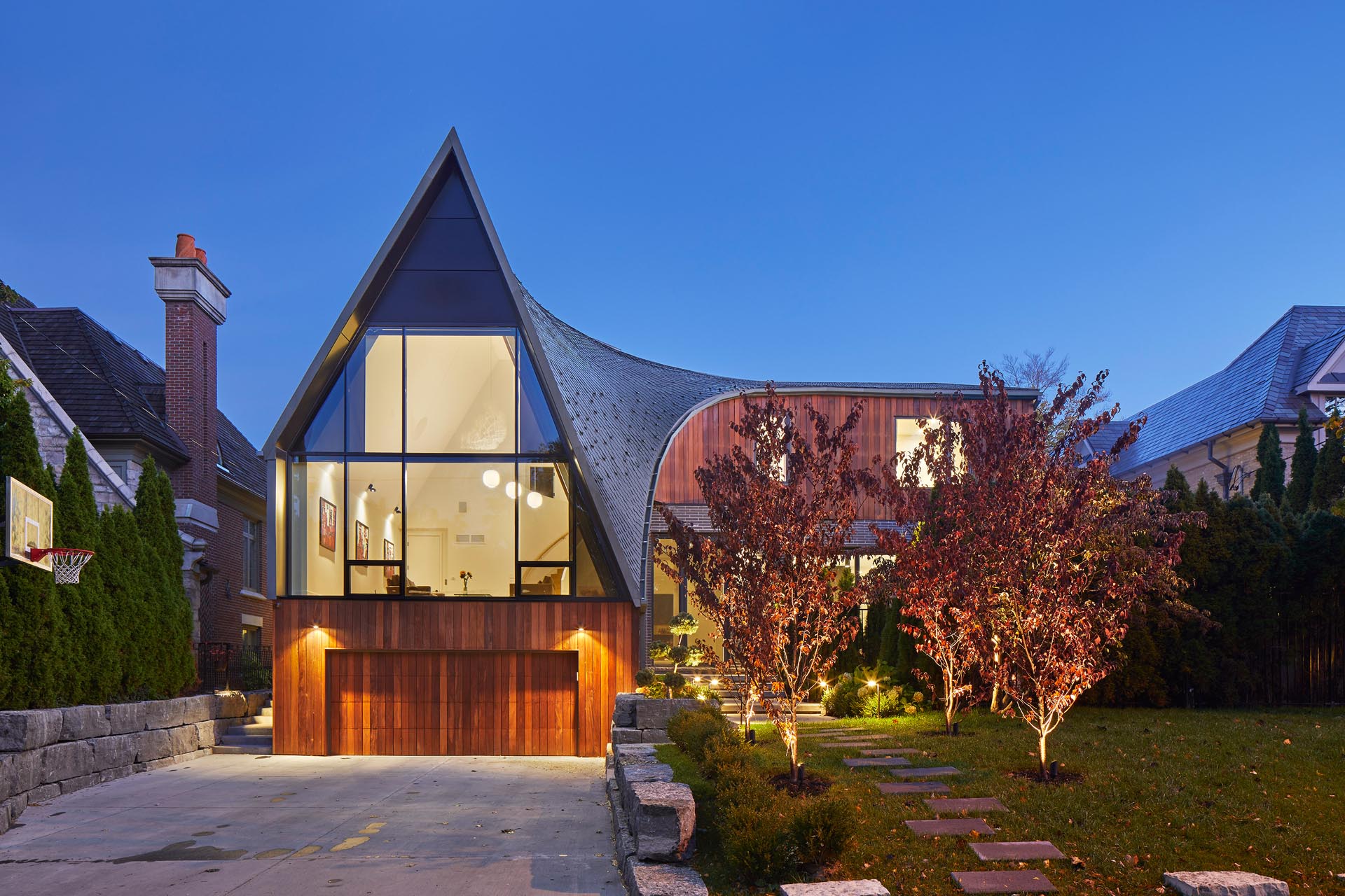 A modern home with a curved roof, an L-shaped design, and a A-frame accent.