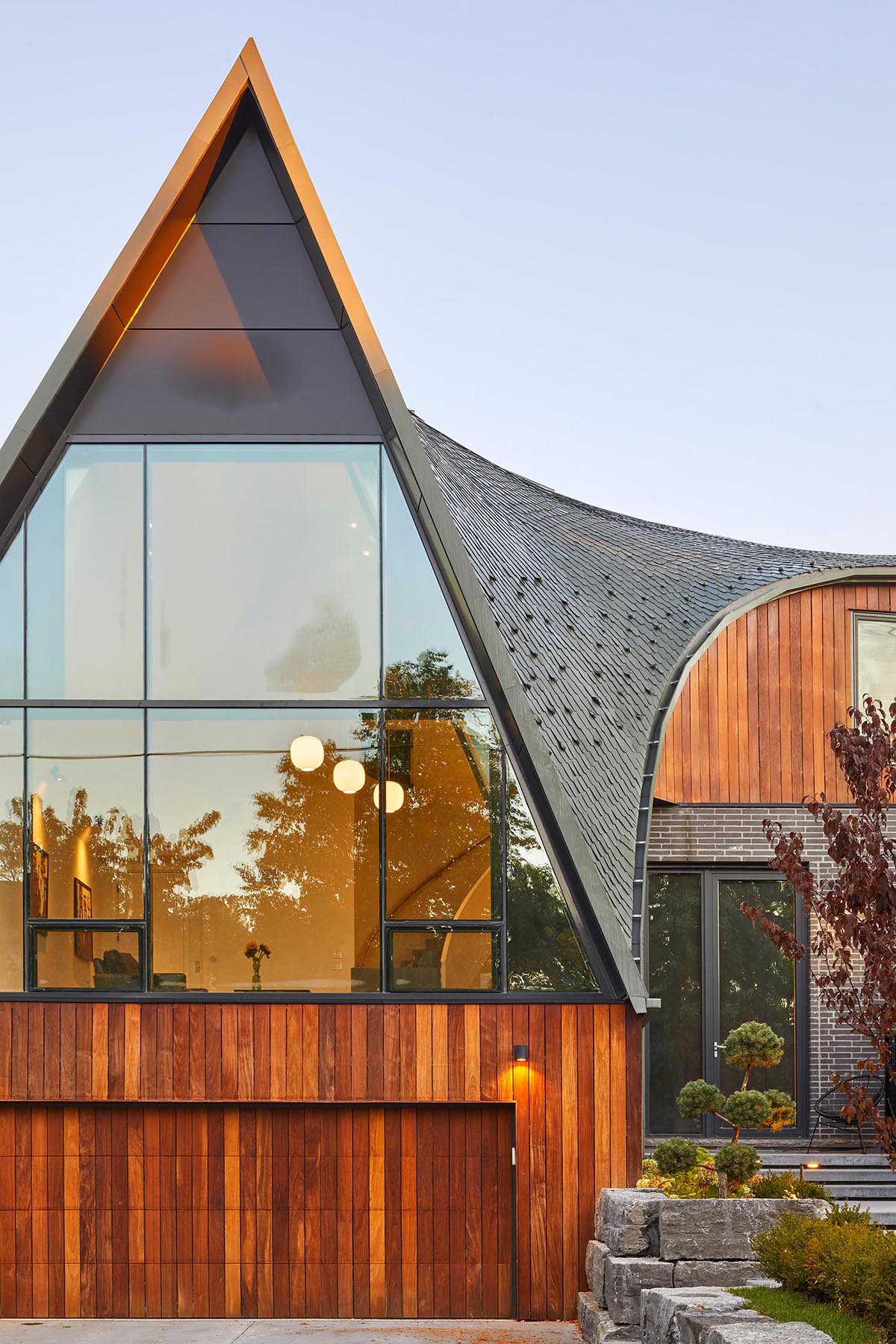 The facade of this modern home with a curved roof features Ipe and brick, that establish a contemporary palette that compliments the neighboring stone, brick and wood homes.