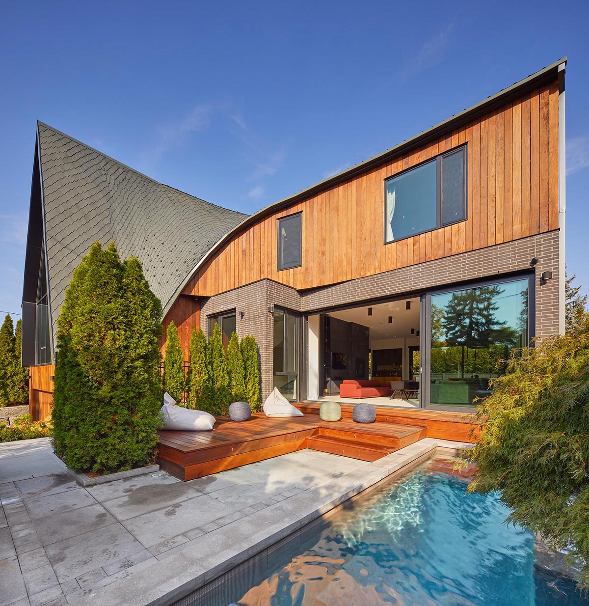 A modern home with a curved roof has a small front courtyard with a swimming pool and sun deck.