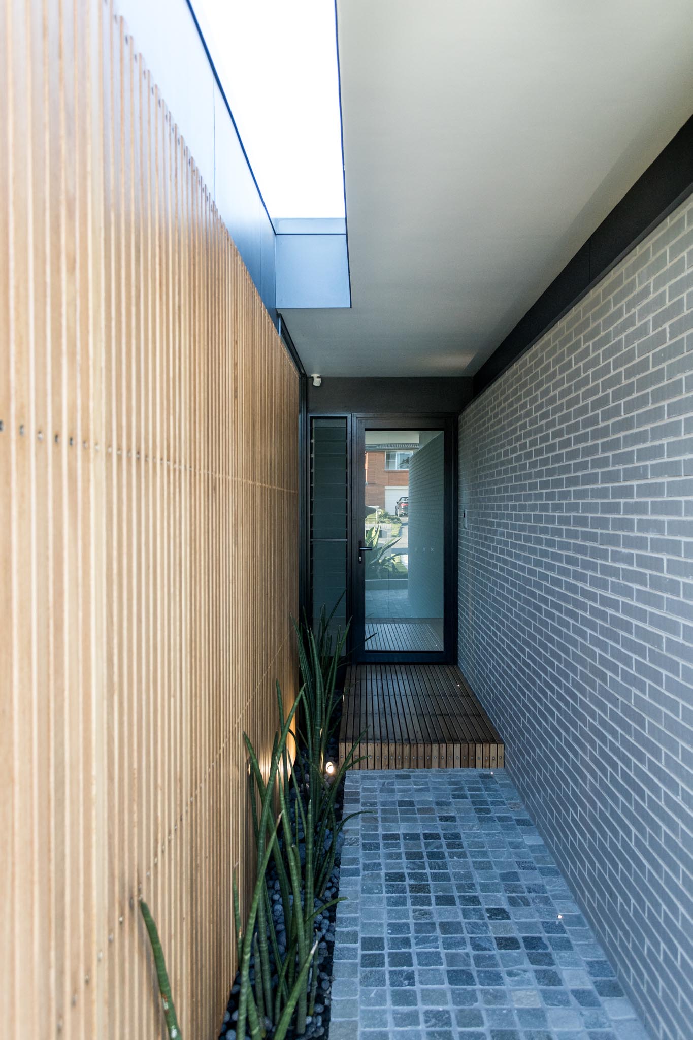 The covered entryway to this modern home is sandwiched between the wood slat wall and the new gray brick wall.