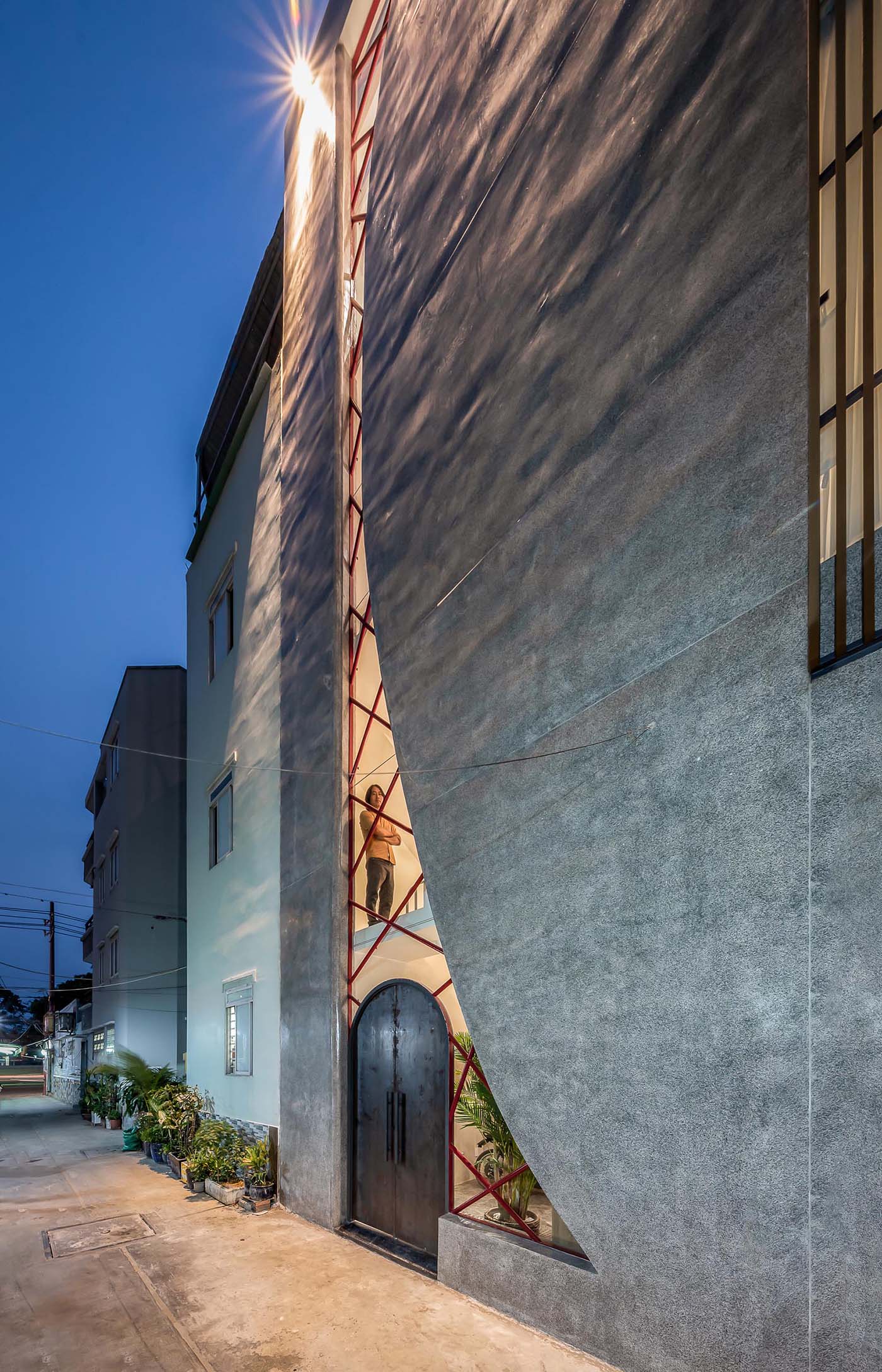 A modern concrete house with an irregular shaped window, also incorporates the steel arched front door.