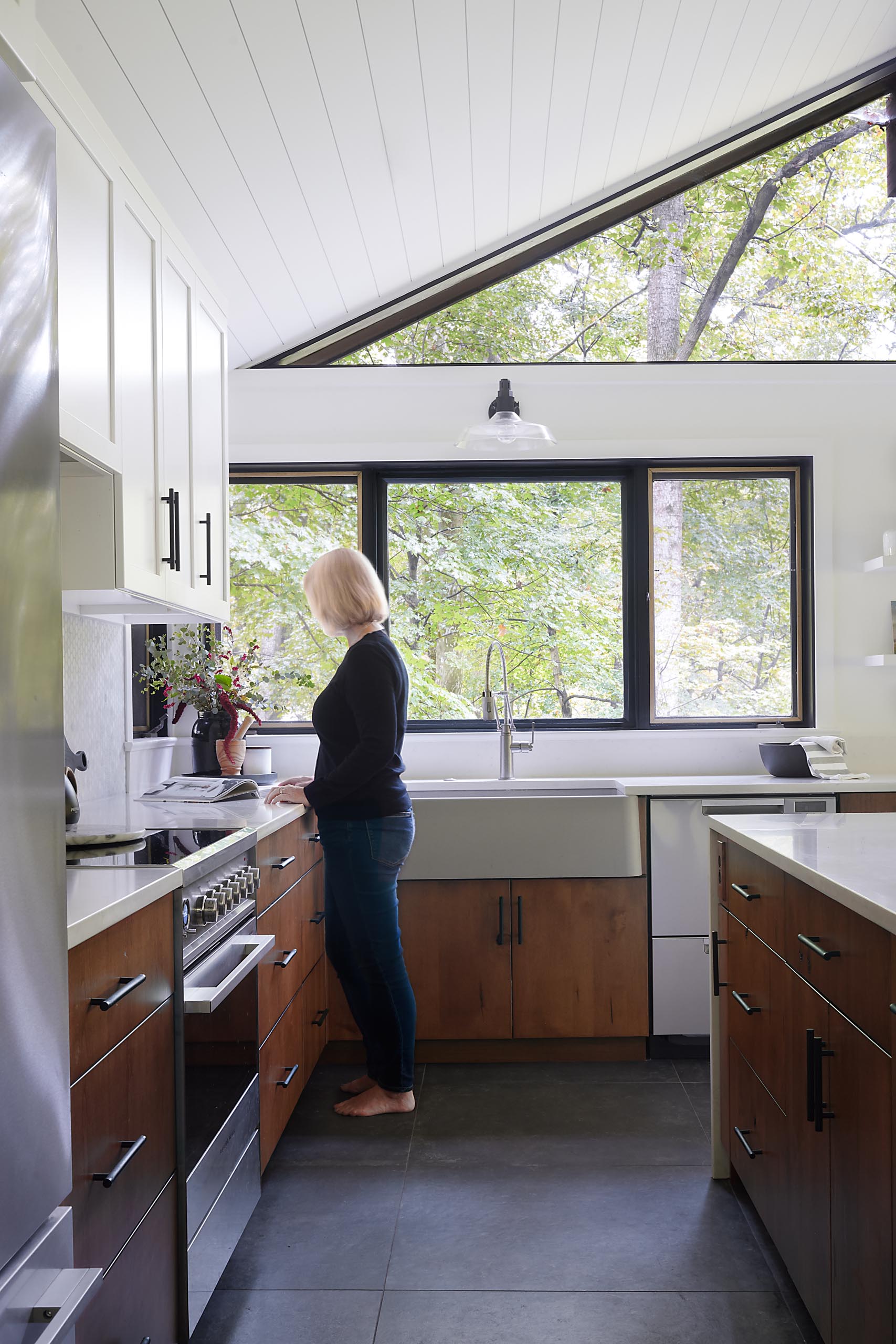 A modern kitchen with white countertops, wood and white cabinets, black hardware, and an apron sink.