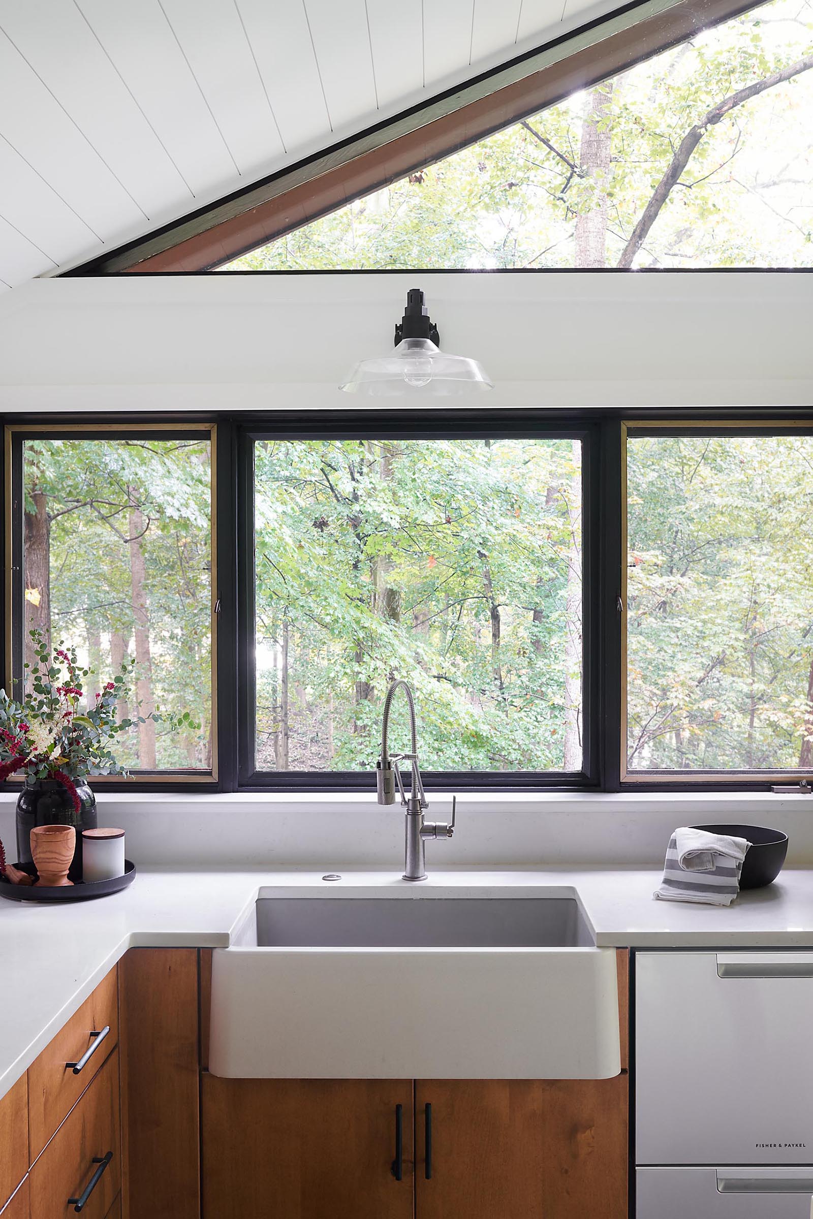 A modern kitchen with white countertops, wood cabinets, and an apron sink.