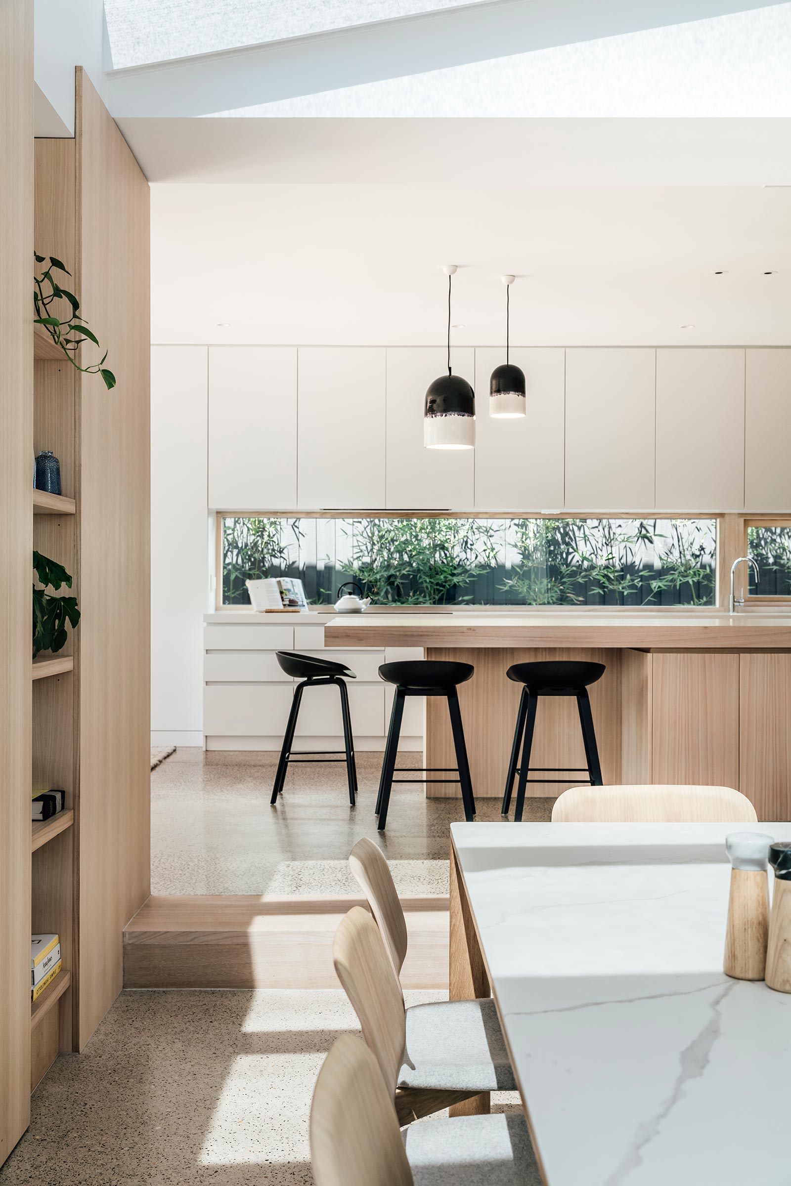 A modern kitchen with minimalist white and wood cabinets, and a window that acts as a backsplash.