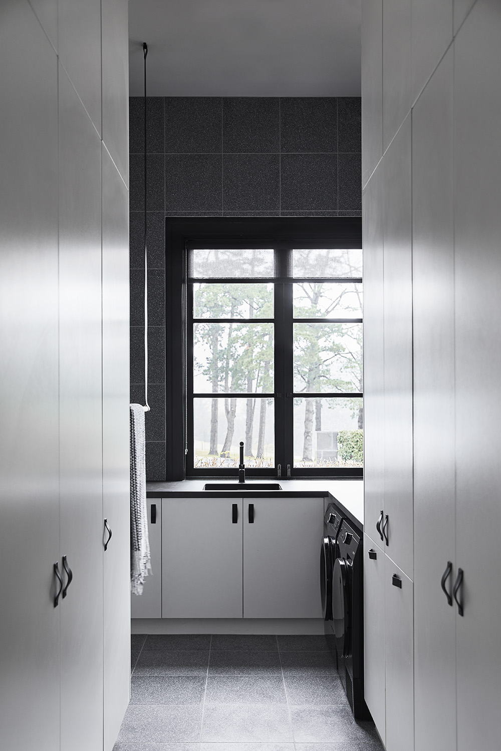 A modern laundry room with floor-to-ceiling tiles, plenty of storage cabinets, as well as hanging bars for drying delicate items.