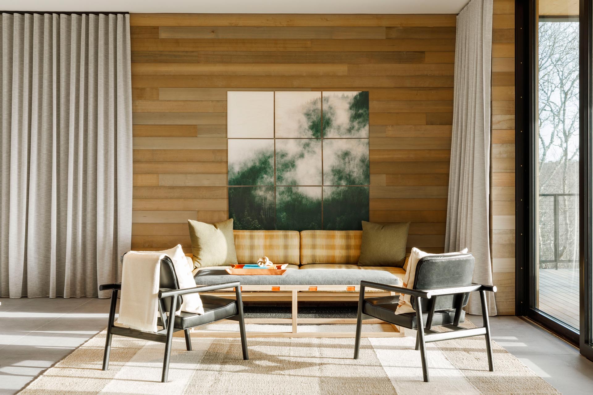 A modern living room with comfortable furnishings, floor-to-ceiling curtains, and wood accent wall.