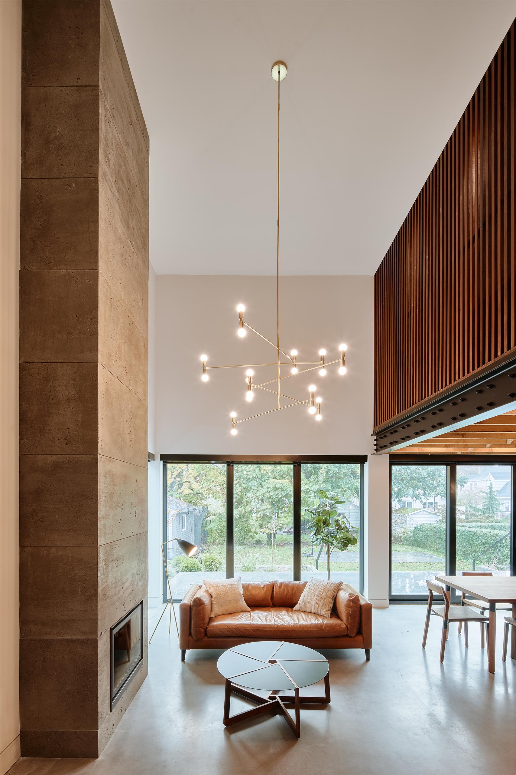 This modern living room has a double height ceiling, a fireplace, and a modern chandelier. 