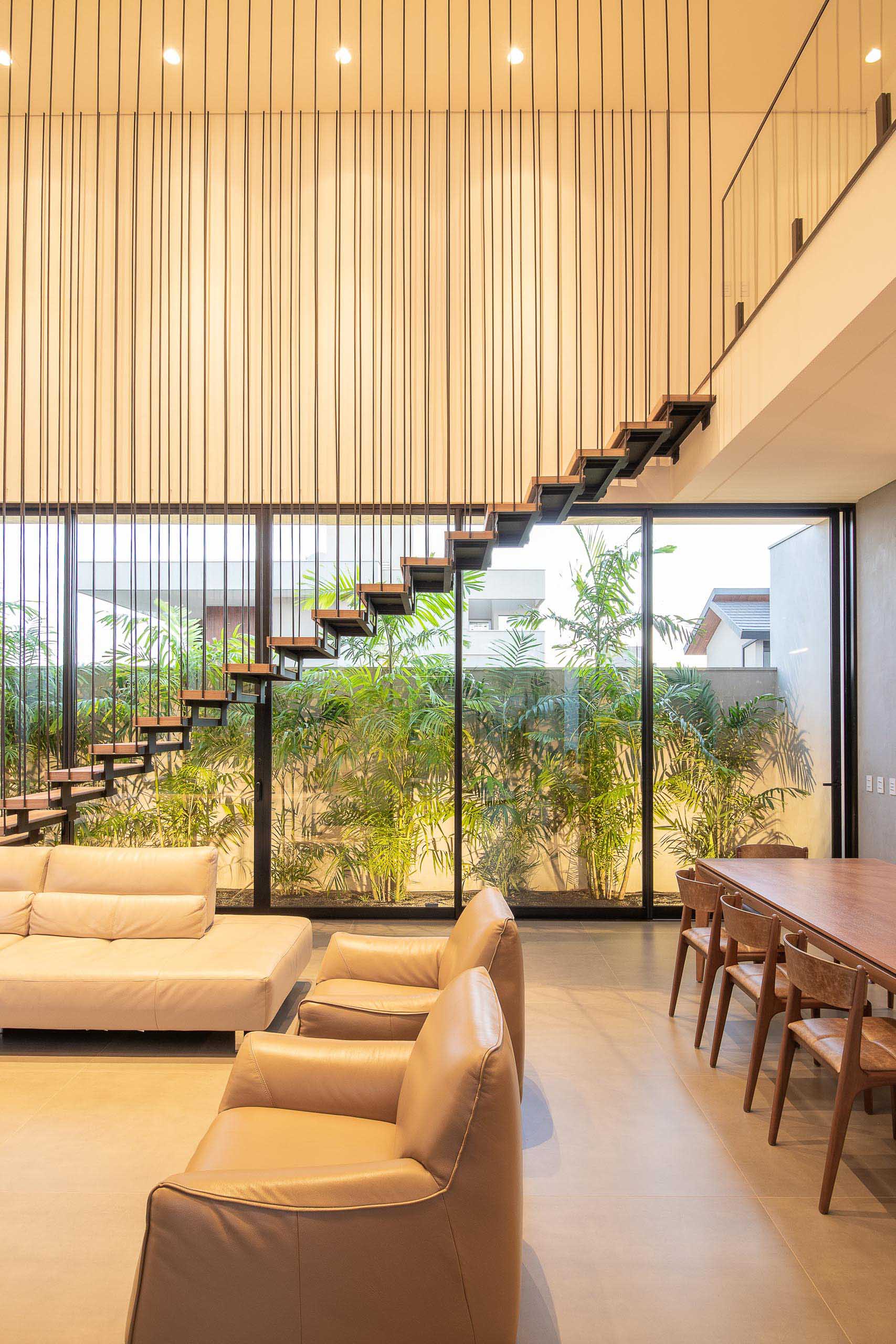 This mdoern living room is flooded with natural light from the oversized windows and sliding doors, while the stairs draw attention to the double height ceiling.