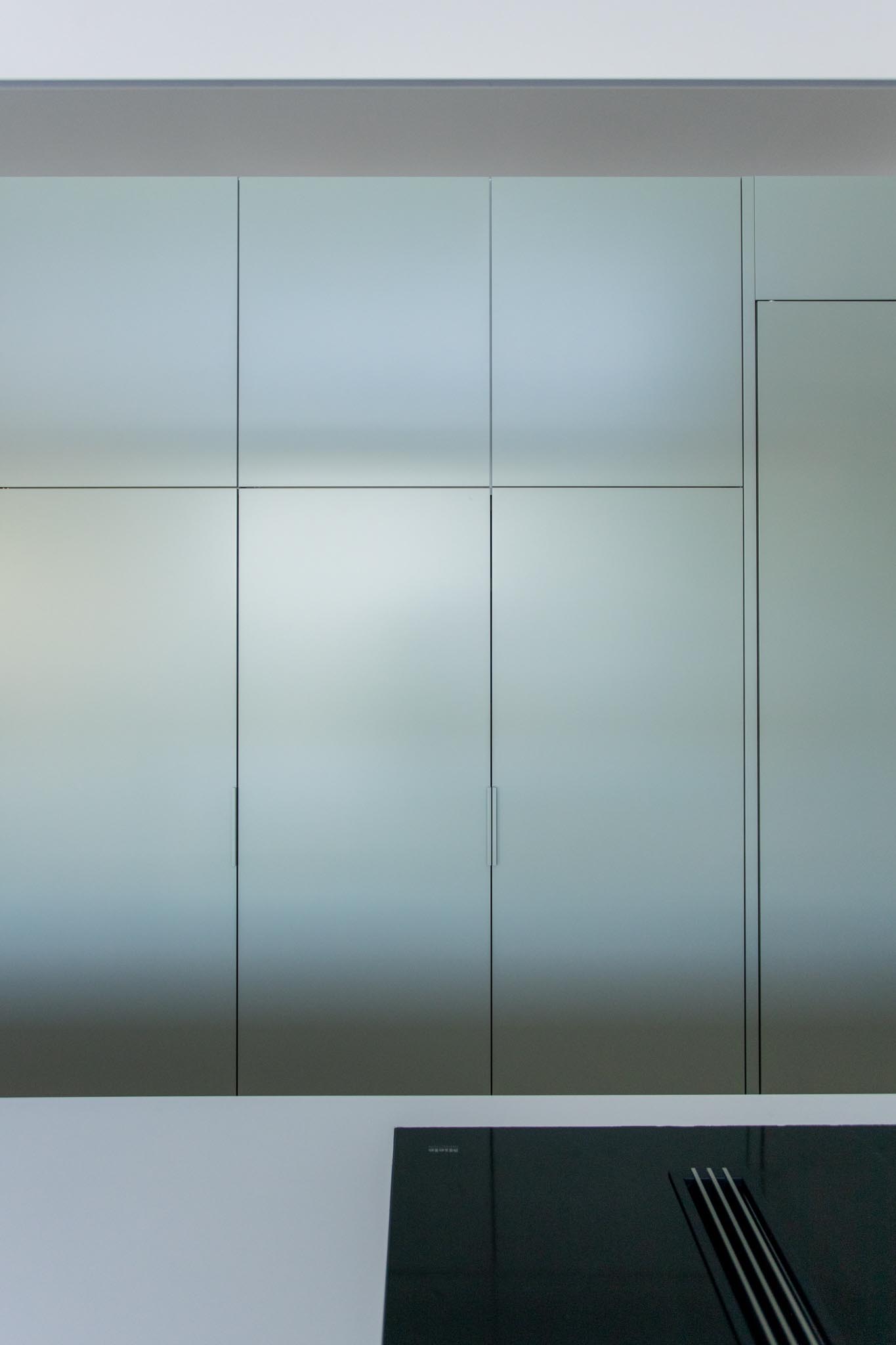 This kitchen has a minimalist design that includes an integrated fridge, and a large white island with wood detailing.