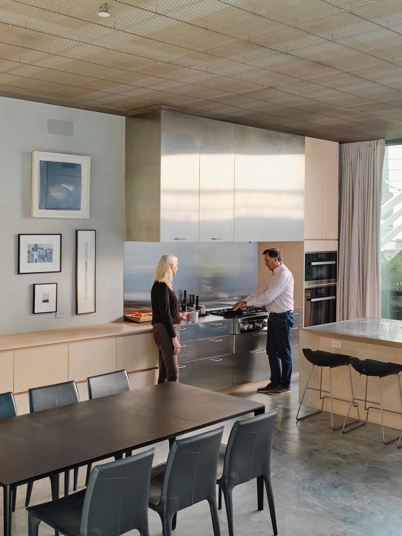 This modern open plan kitchen and dining room includes high ceilings, as well as light wood and stainless steel cabinets.