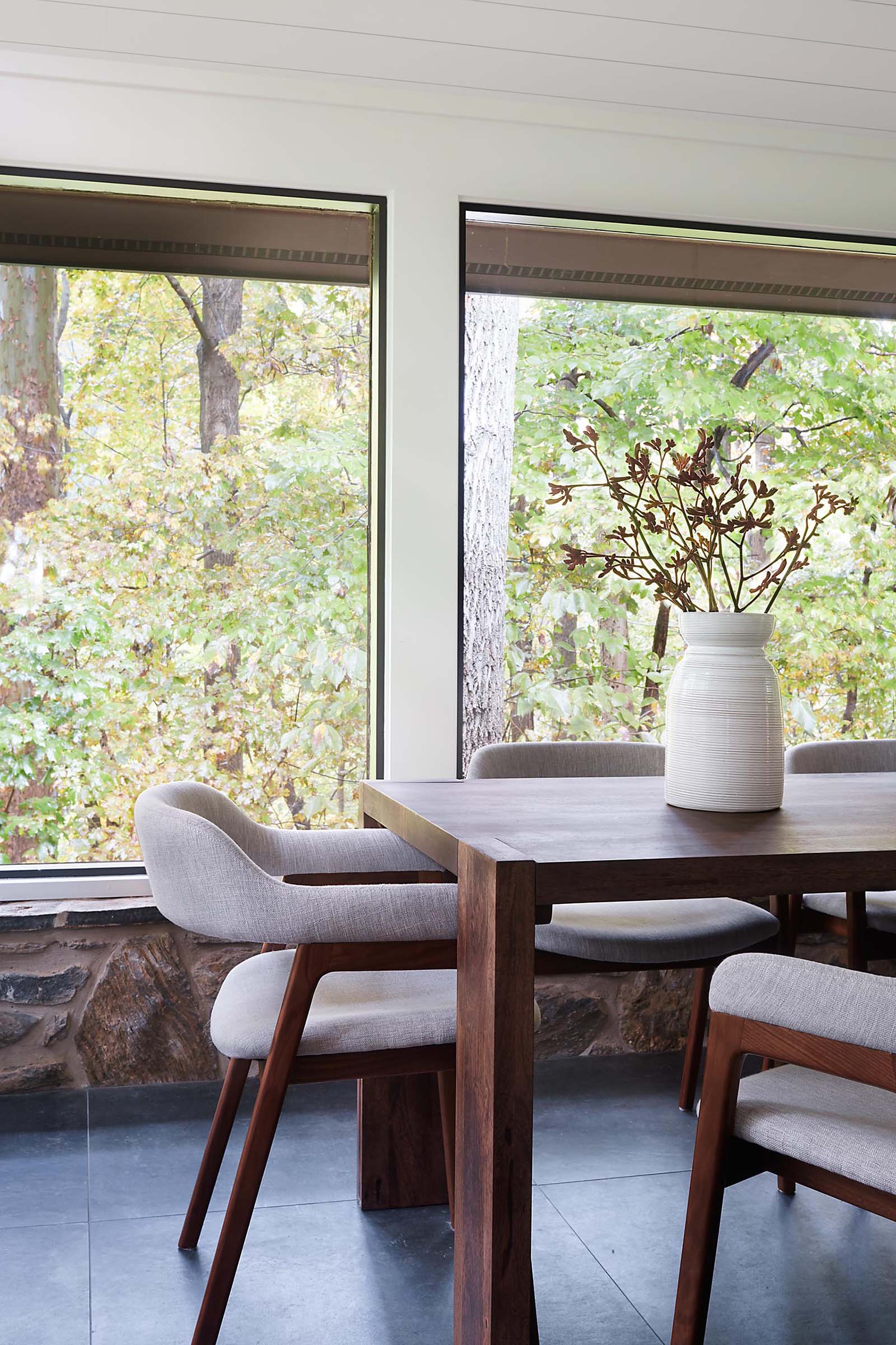 A modern dining room surrounded by windows has large format floor tiles.