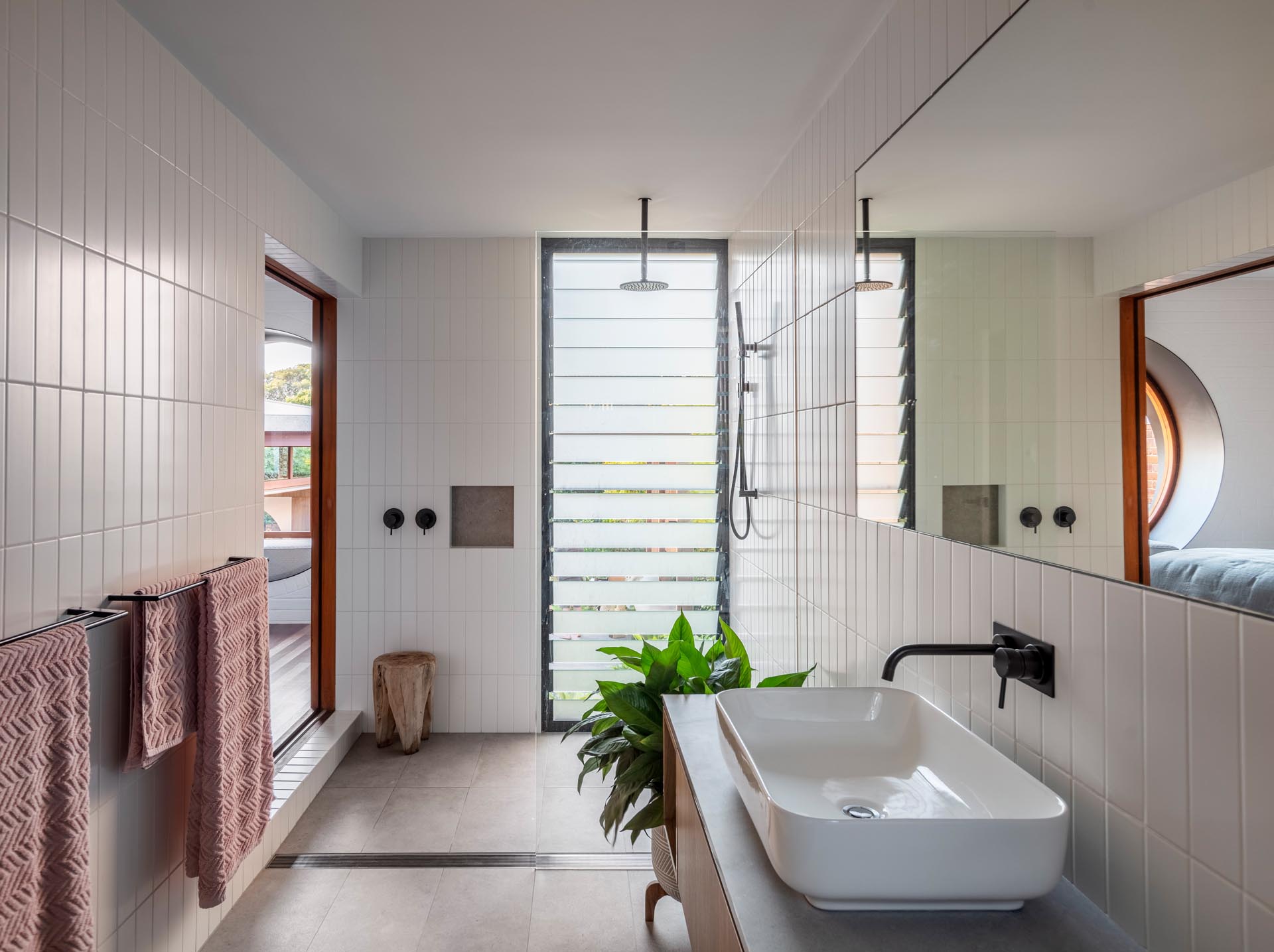 A modern bathroom with white rectangular tiles and a louver window in the shower.