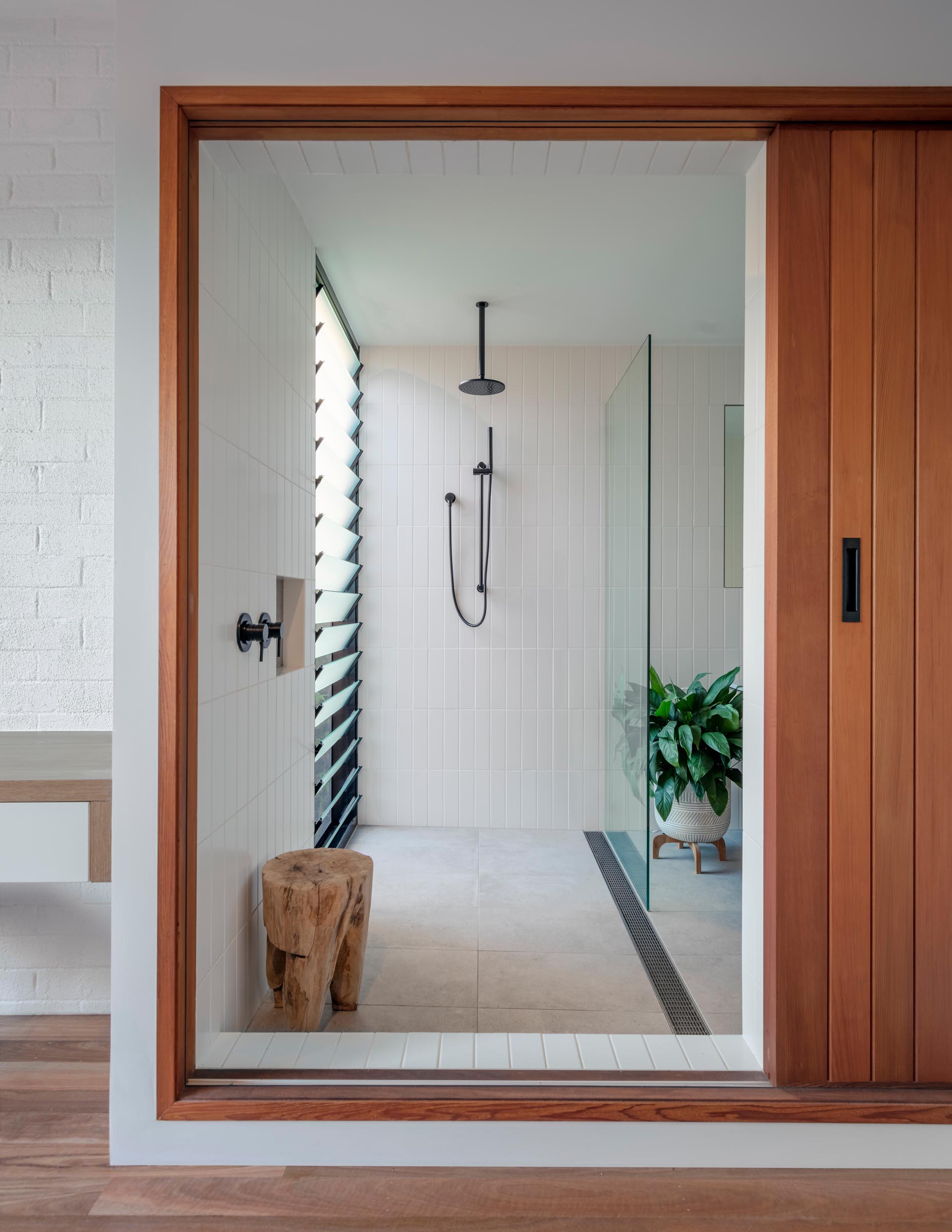 A modern bathroom with white rectangular tiles and a louver window in the shower.