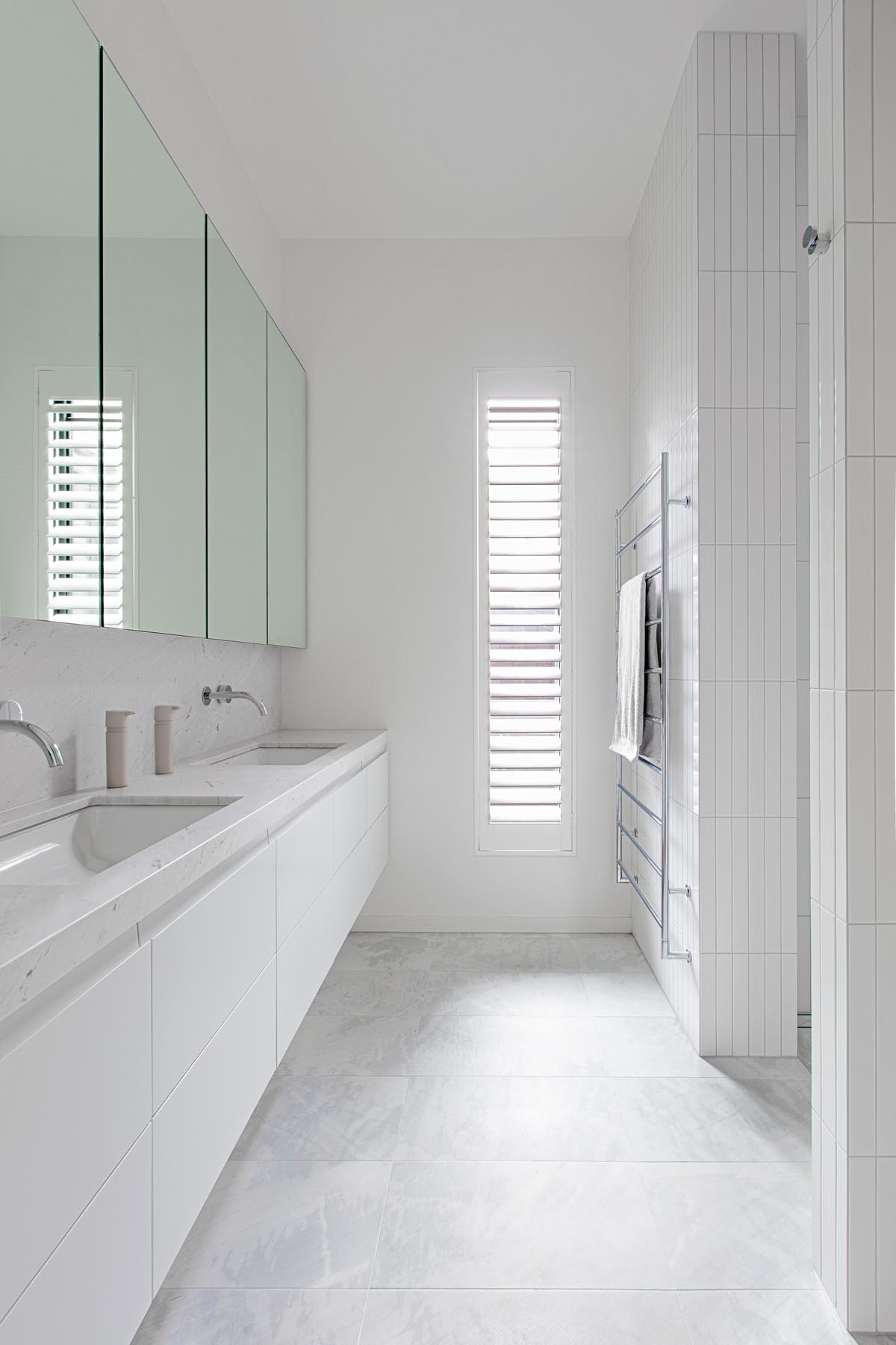 In this modern all white bathroom, honed Carrara Bianco marble was used for both the vanity countertop and the flooring.