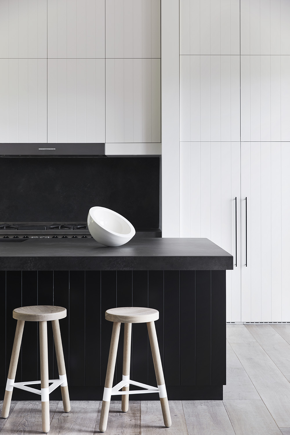 In this modern kitchen, there's minimalist white cabinets with integrated appliances, as well as a large black island that measures in at almost 10 feet (3m), and includes a black stone countertop that overhangs to provide room for seating.