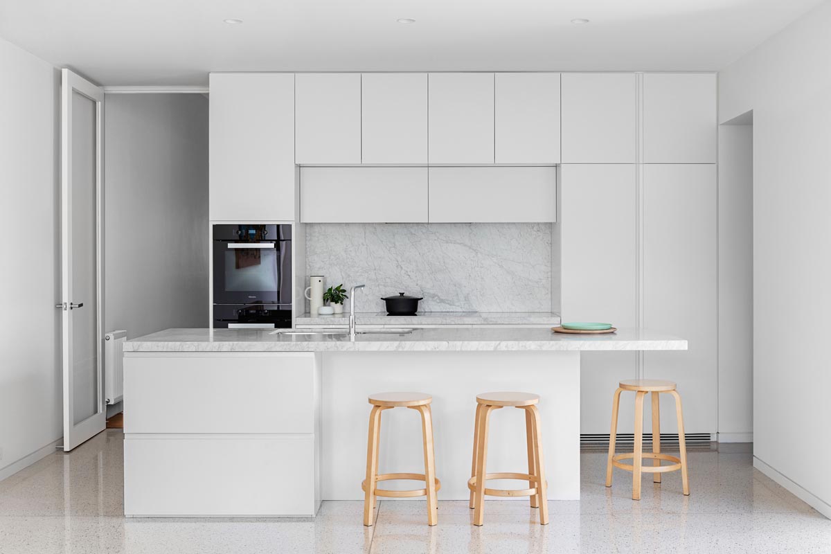 In this all-white kitchen, minimalist hardware free white cabinets have been paired with complementing honed Elba countertops.