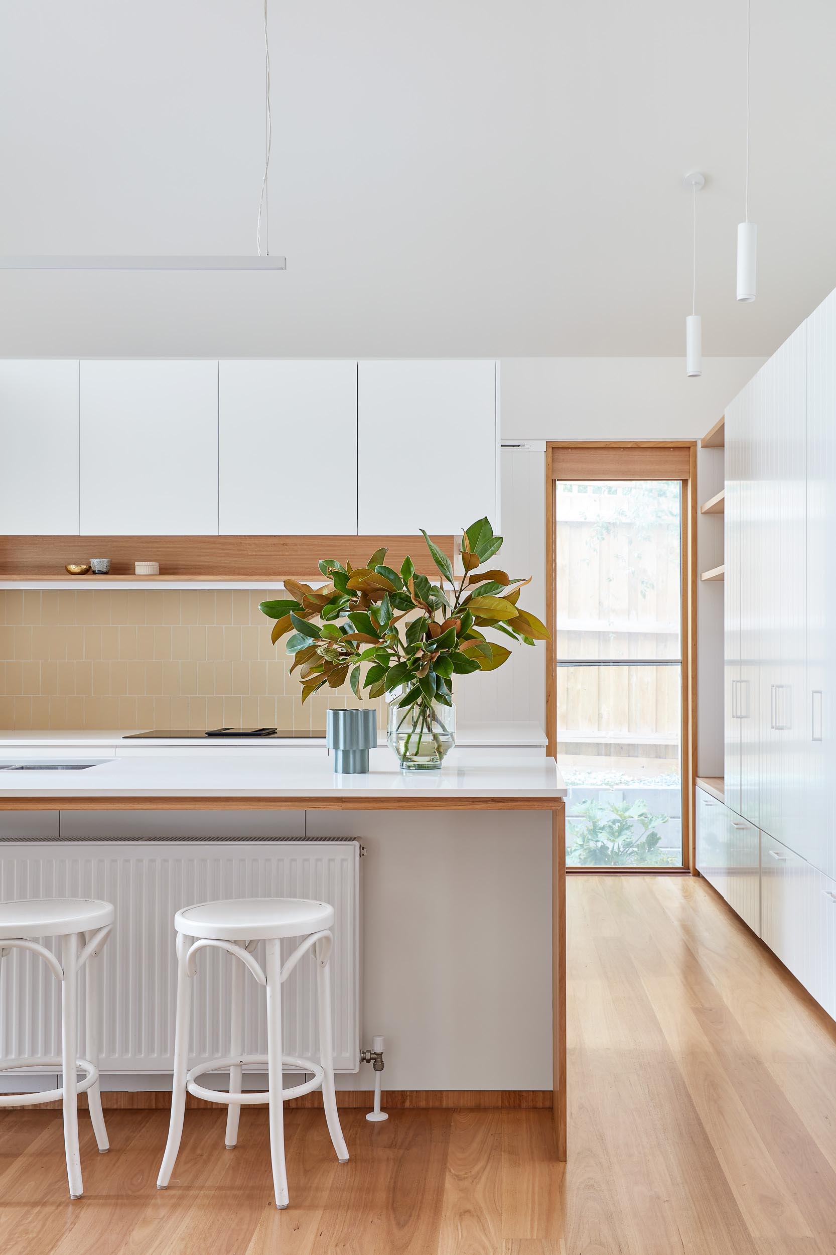 In this modern kitchen, minimalist white cabinets are complemented by the Glacier White Corian countertops and Blackbutt Timber accents.