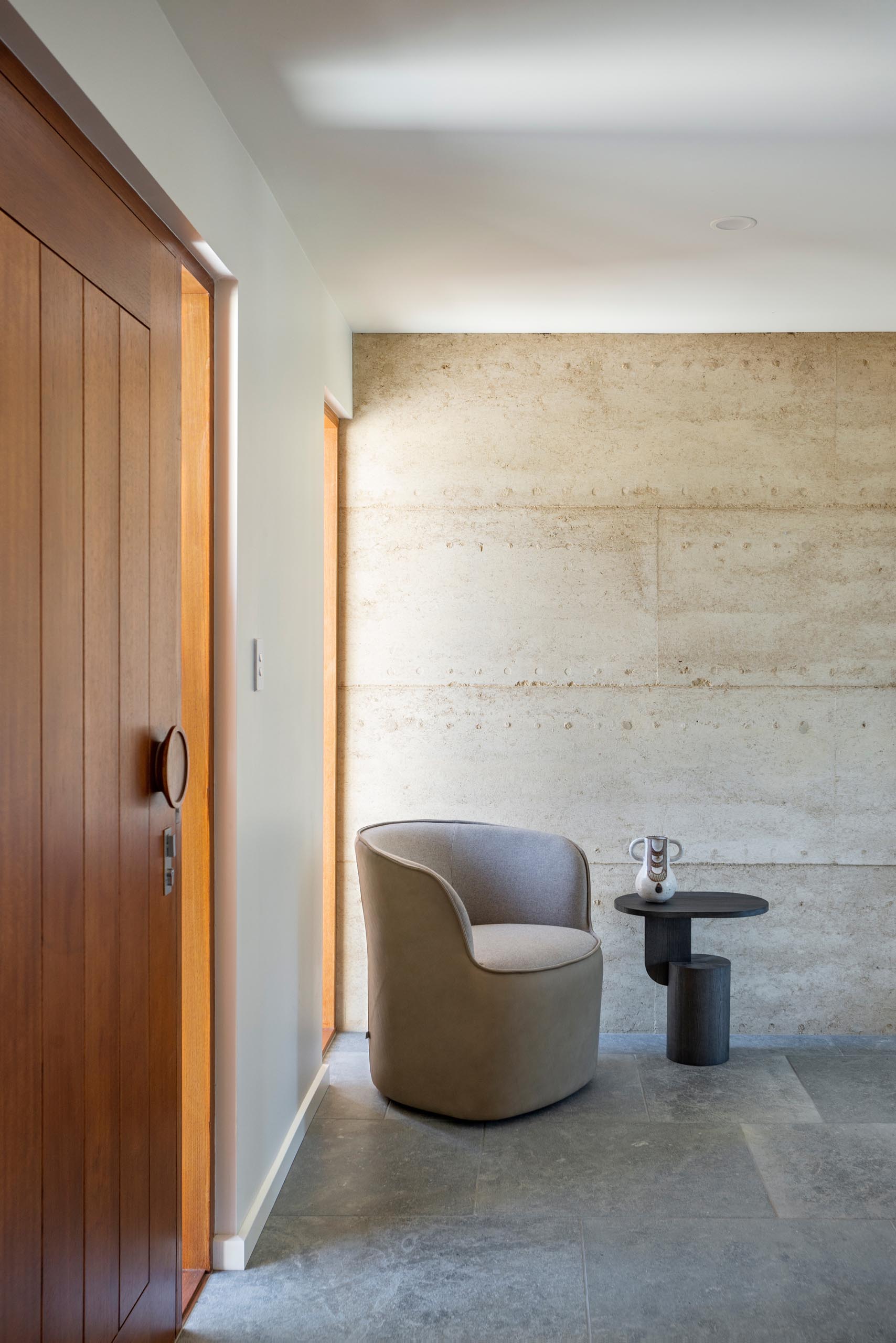 A modern entryway with a wood front wood and a rammed earth wall.