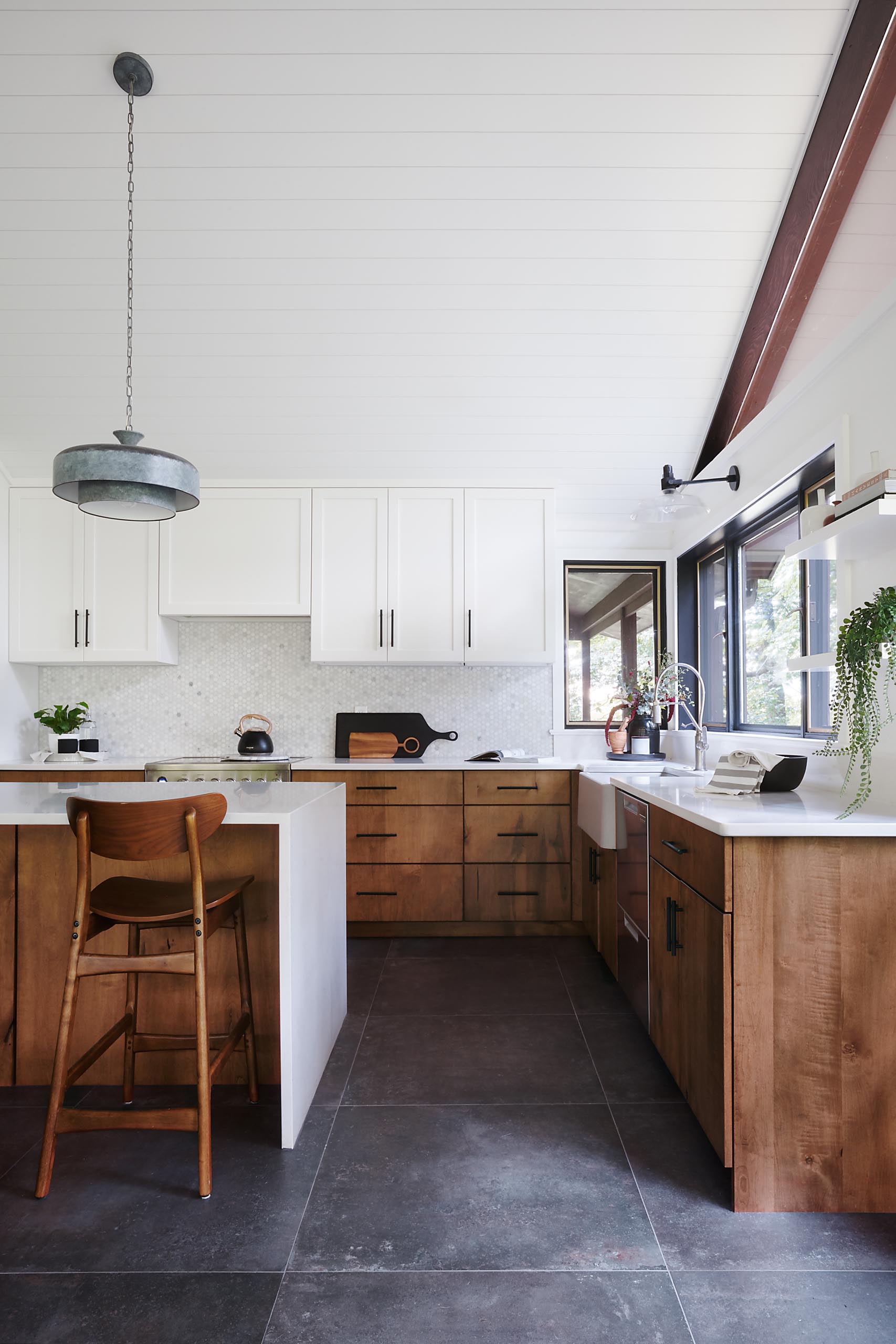 A modern kitchen with white countertops, wood and white cabinets, black hardware, and an apron sink.