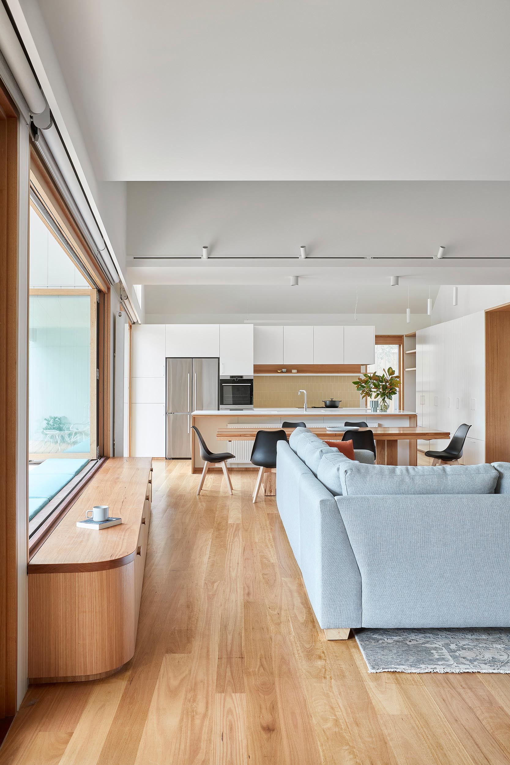 A modern living room has a bench below a series of windows that open to connect the interior with the bench on the other side of the windows.