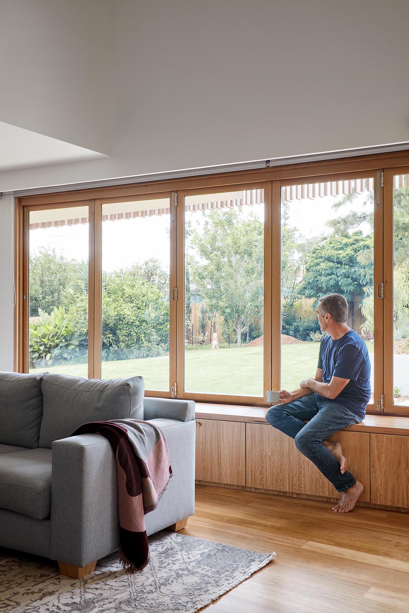 A modern living room has a bench below a series of windows that open to connect the interior with the bench on the other side of the windows.