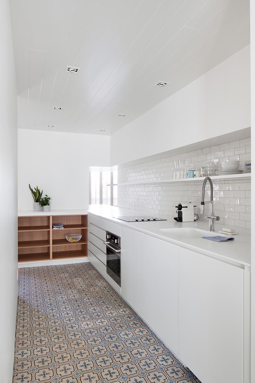 A modern and mostly white kitchen has wood shelf accents and colorful patterned tiles.