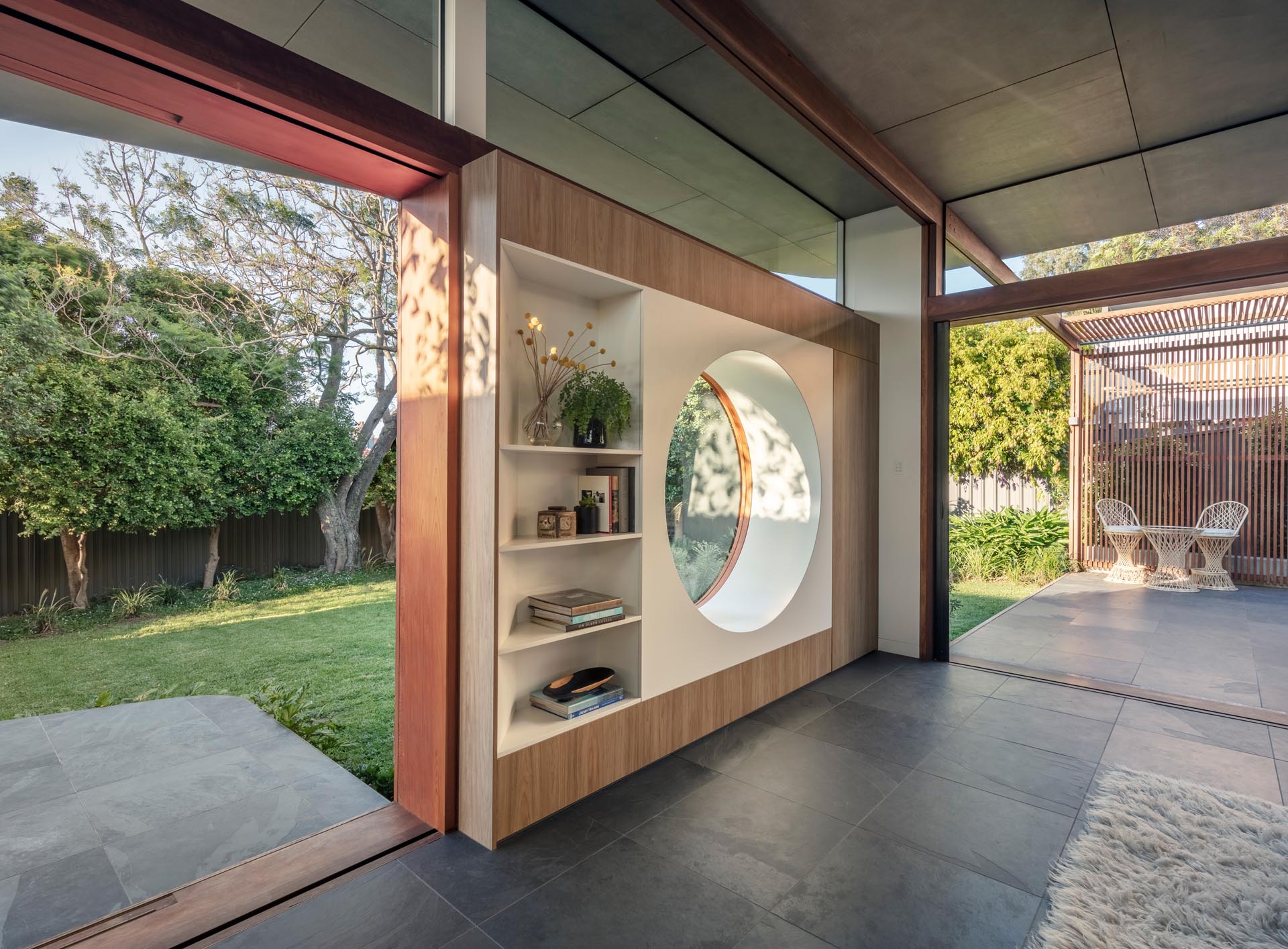 A modern living room with a circular window and built-in shelving.