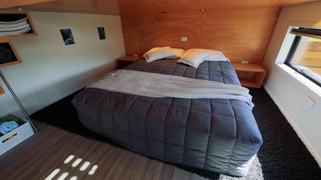 A modern tiny home with an open bedroom that includes a roll-out bed that makes it easier to change the bedding.