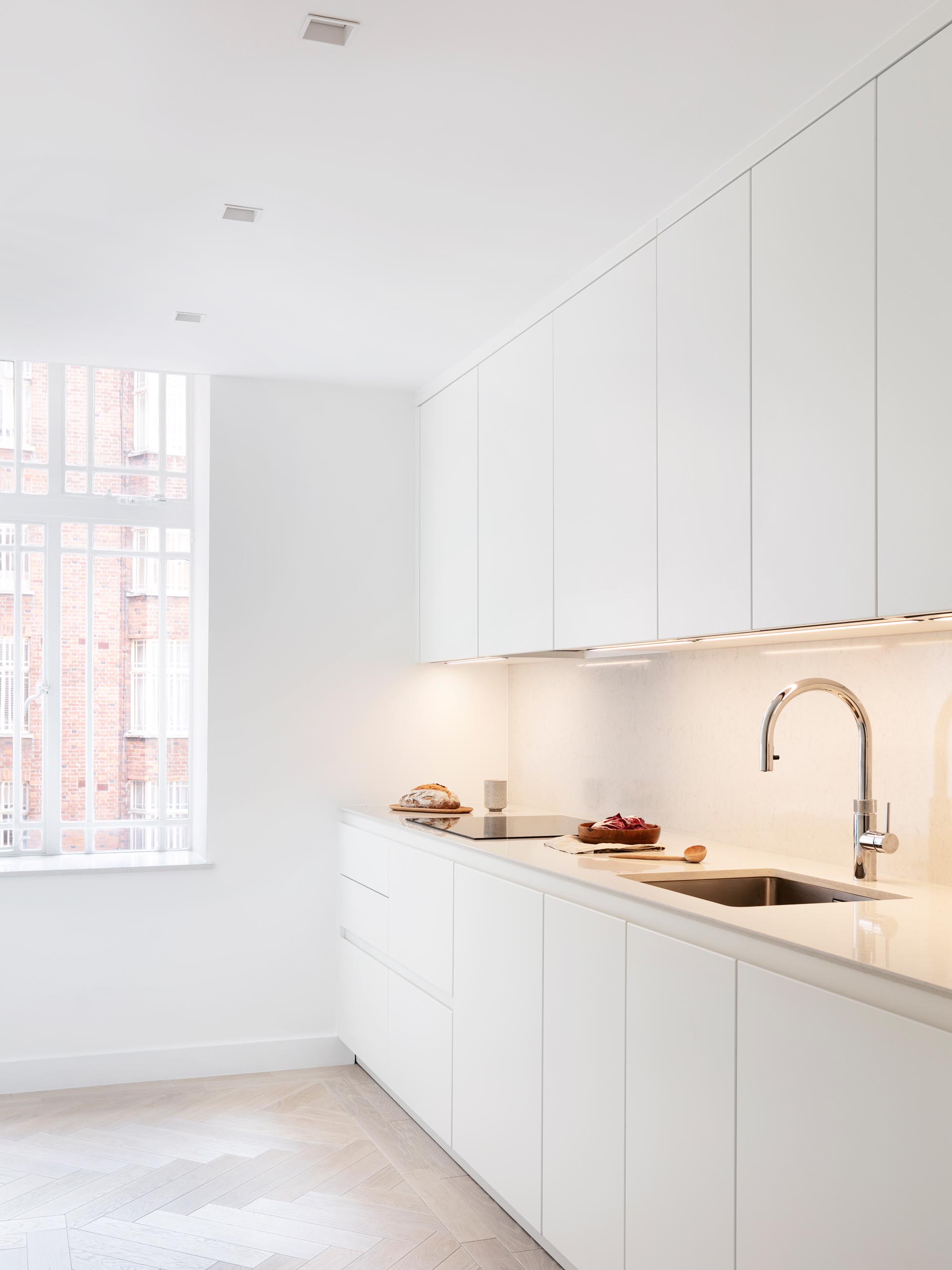 In this modern kitchen, lighting has been installed underneath the minimalist white cabinets, lighting the backsplash and countertop.