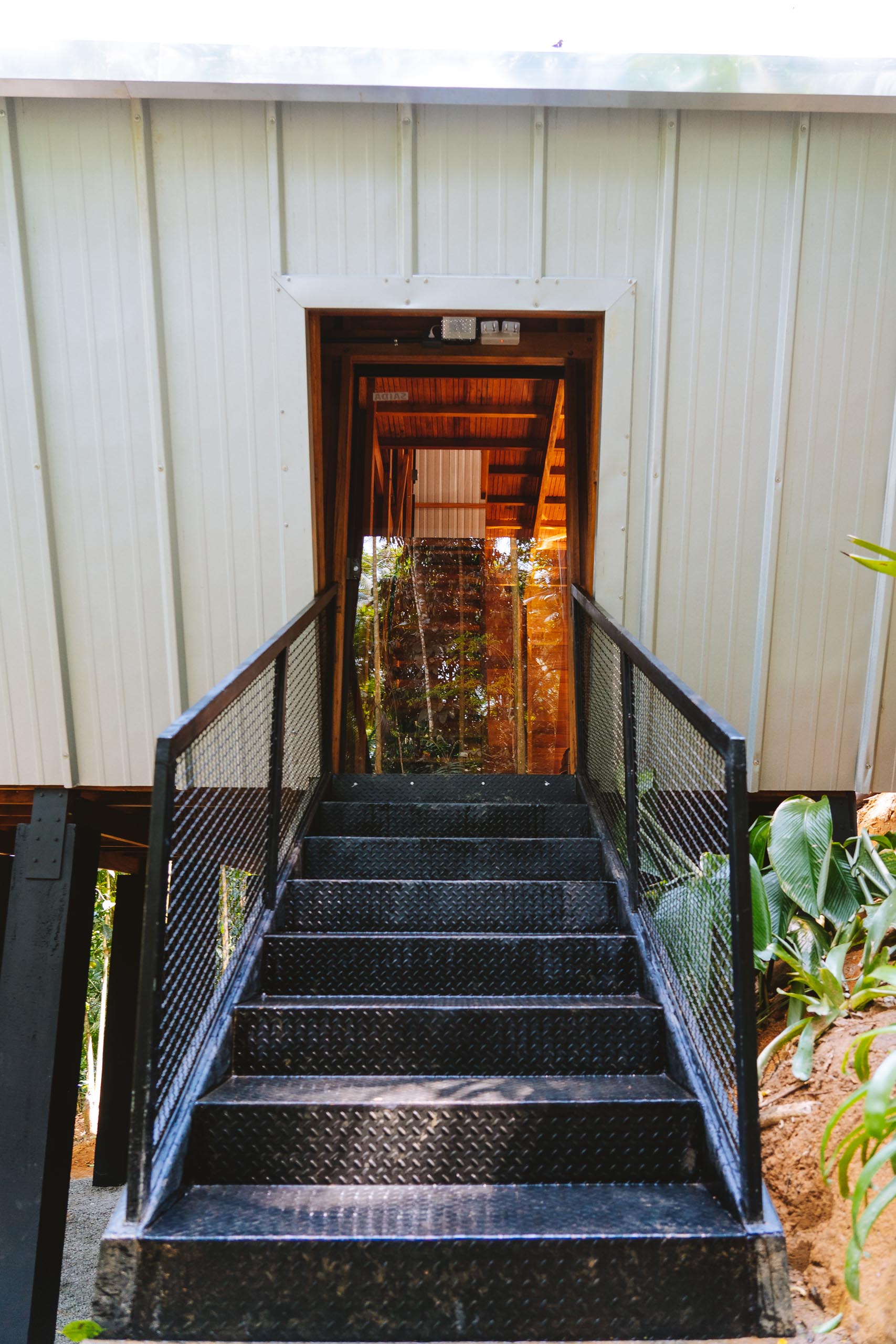 Black metal stairs and handrails provide entry to a raised A-frame cabin.