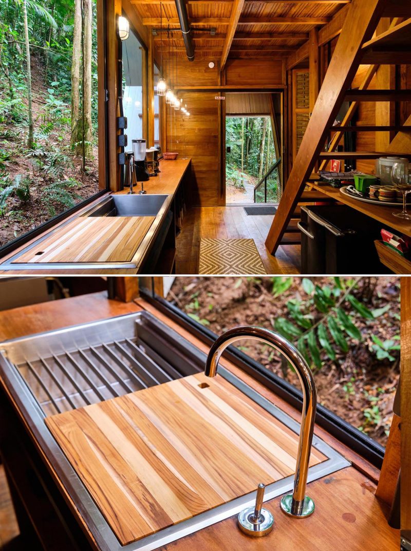 The kitchen of an A-frame cabin with a warm wood interior, includes open shelving and large windows.