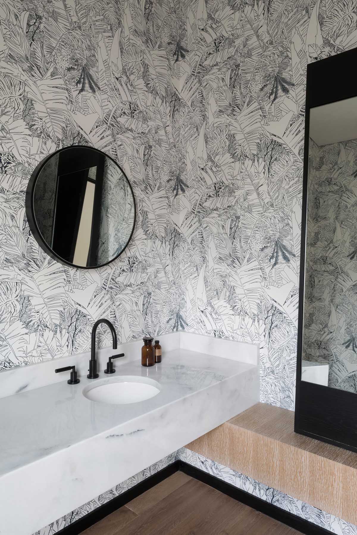 A modern bathroom with black and white tropical print wallpaper.