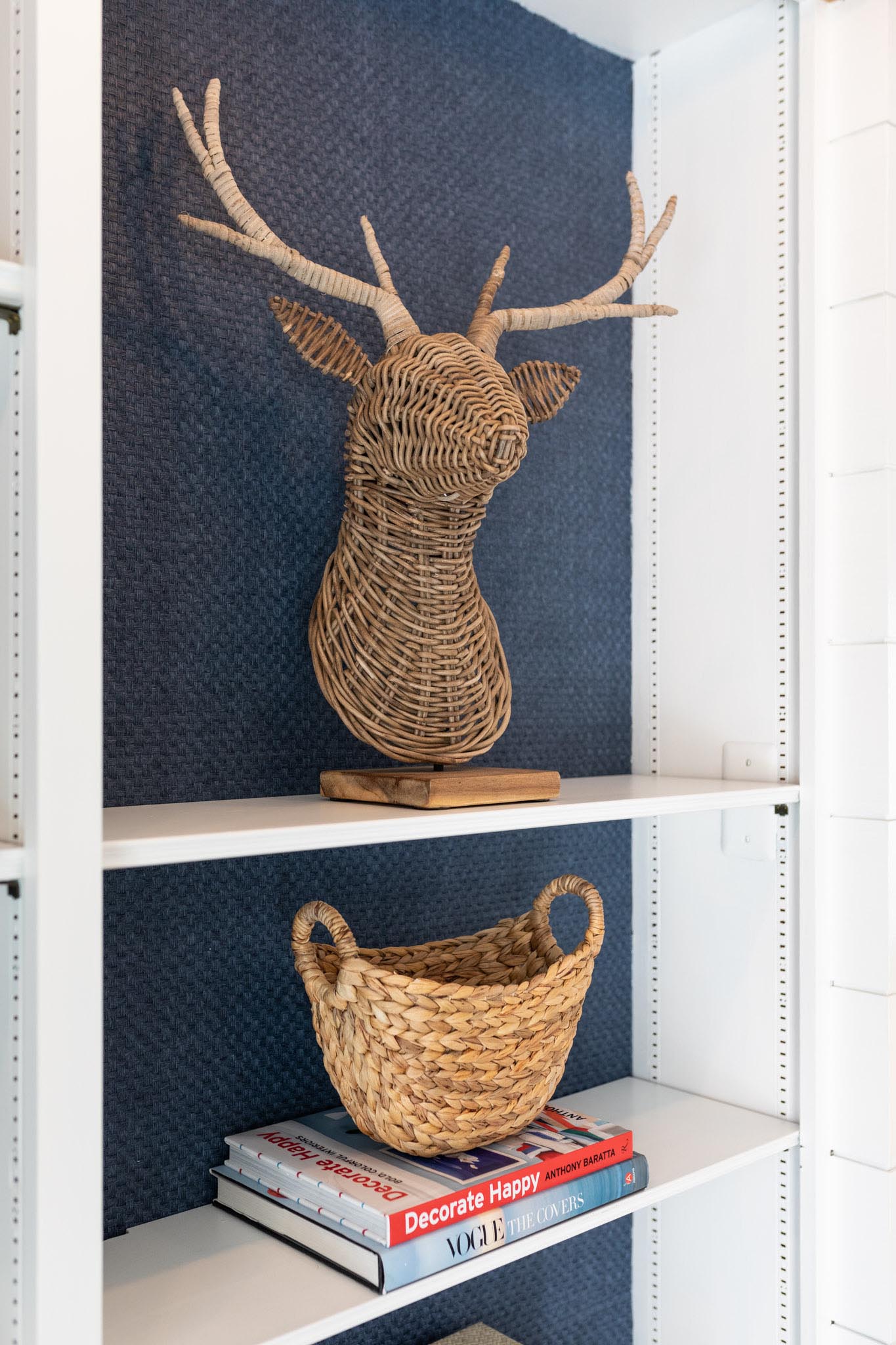 To incorporate texture, the designers of this living room added a blue grass, cloth wallpaper to the walls, that also lines the back of the shelving that are located on either side of the fireplace.