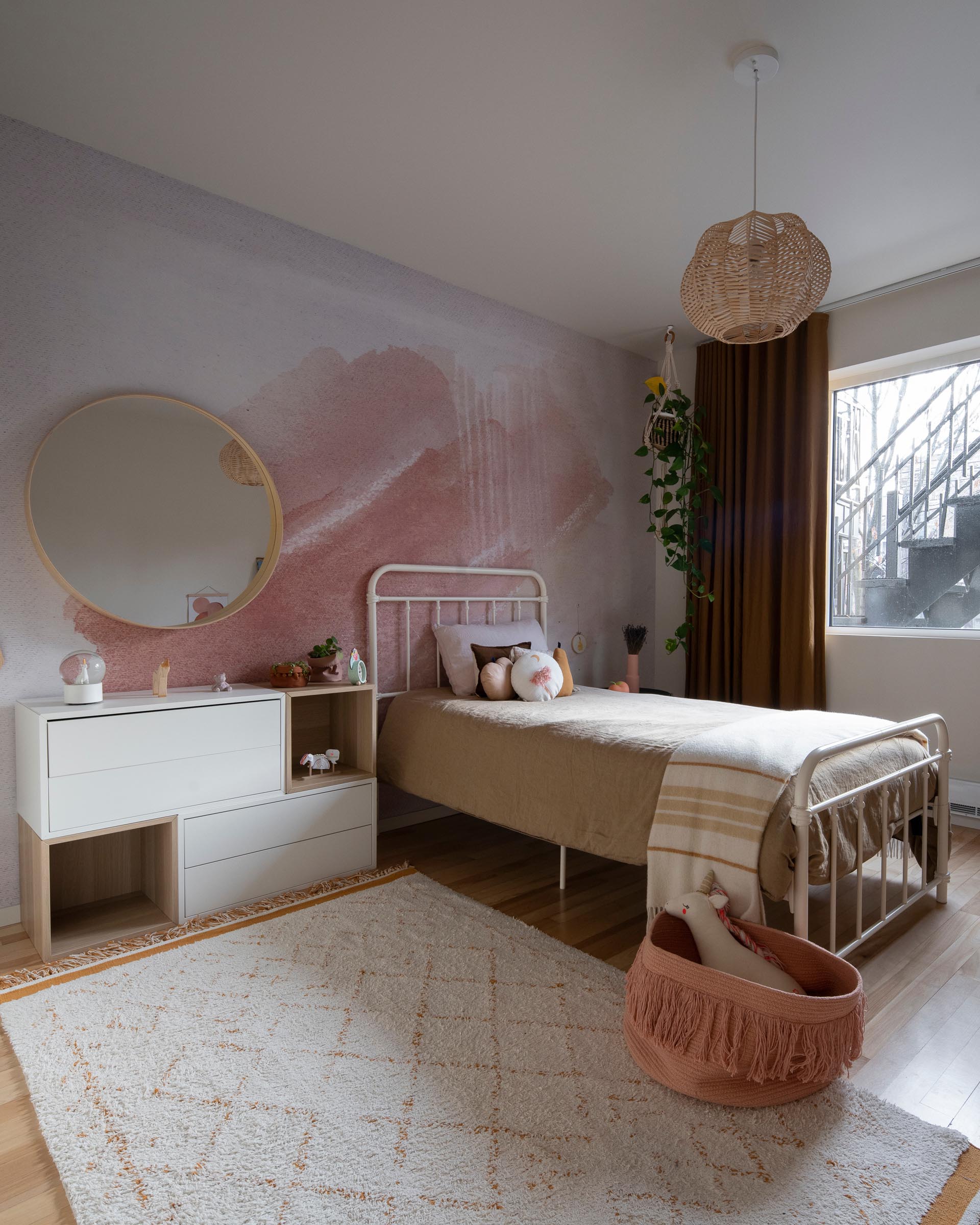 A modern kid's bedroom with a blush-pink and natural palette, and a watercolor wall mural.