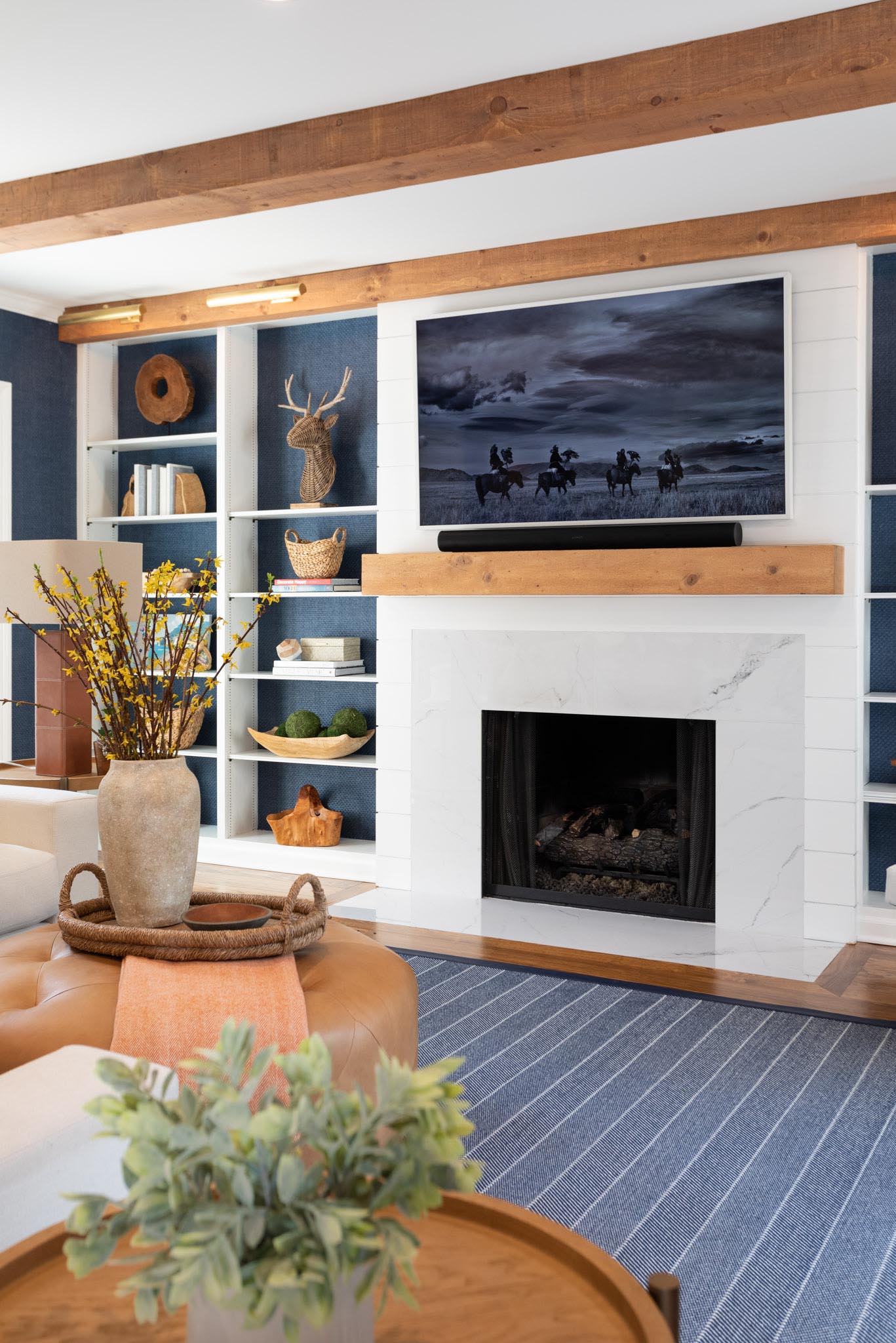 A contemporary living room with a fireplace, plenty of shelves, and walls lined with blue grass, cloth wallpaper.