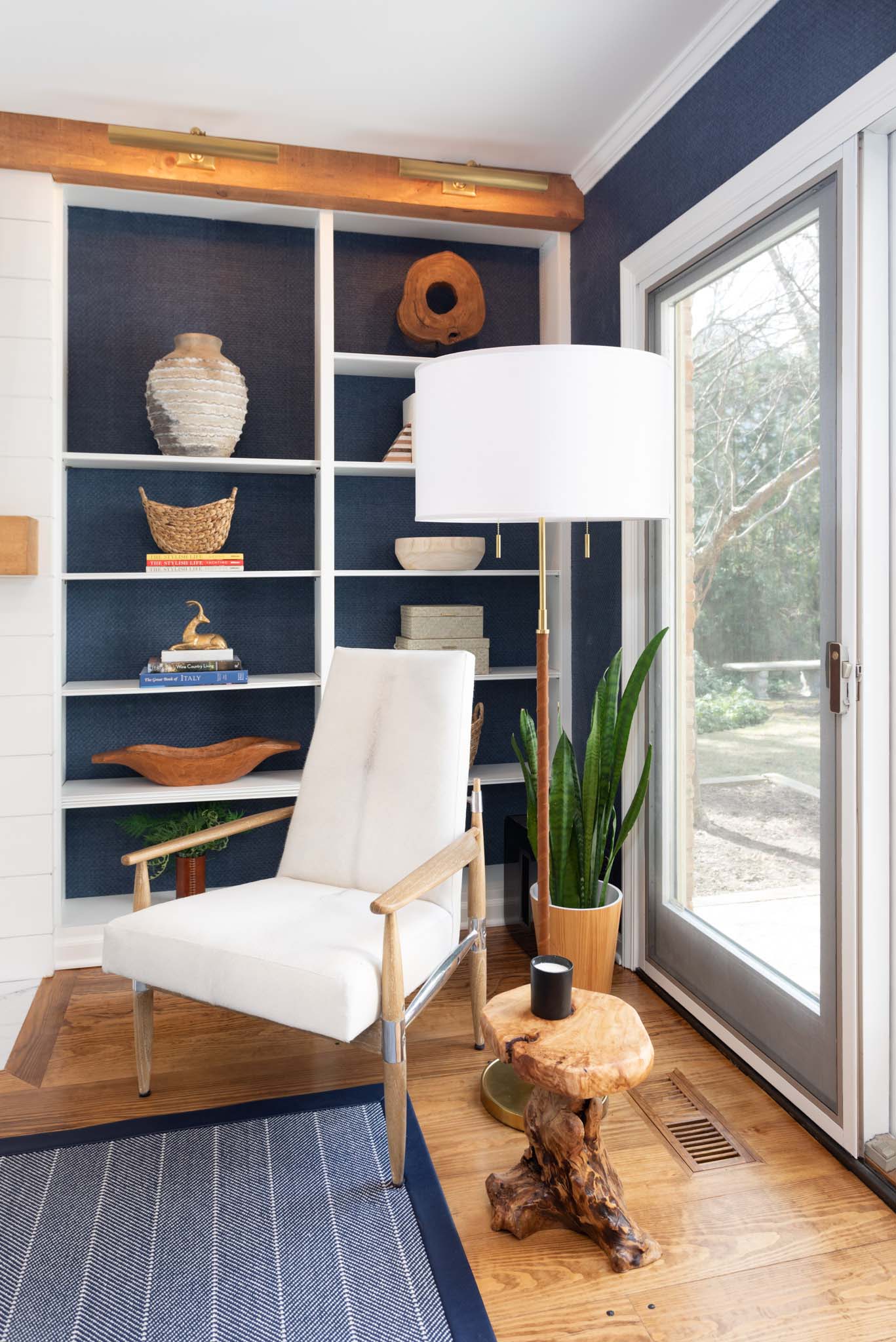 To incorporate texture, the designers of this living room added a blue grass, cloth wallpaper to the walls, that also lines the back of the shelving that are located on either side of the fireplace.