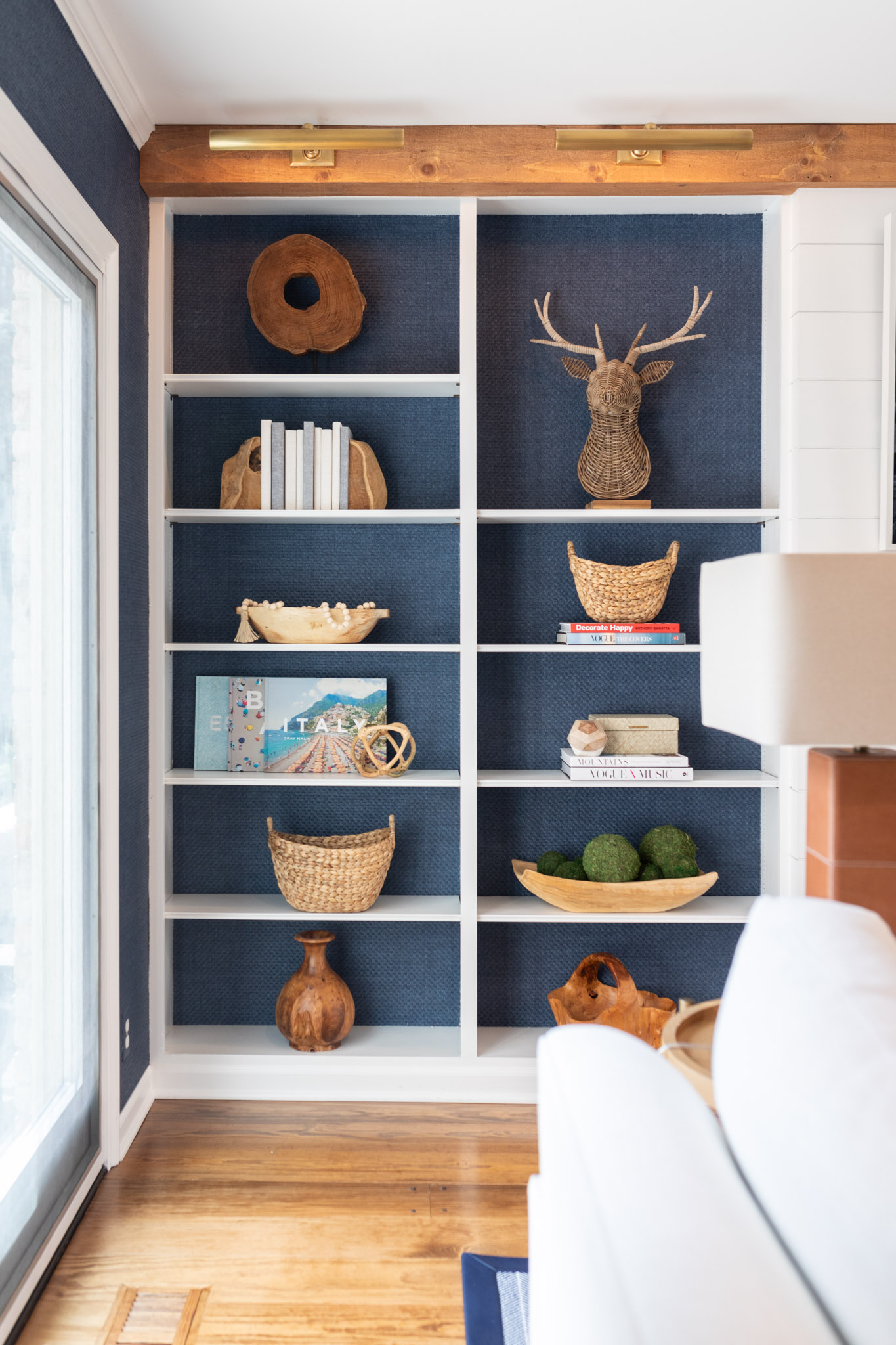 To incorporate texture, the designers of this living room added a blue grass, cloth wallpaper to the walls, that also lines the back of the shelving that are located on either side of the fireplace.