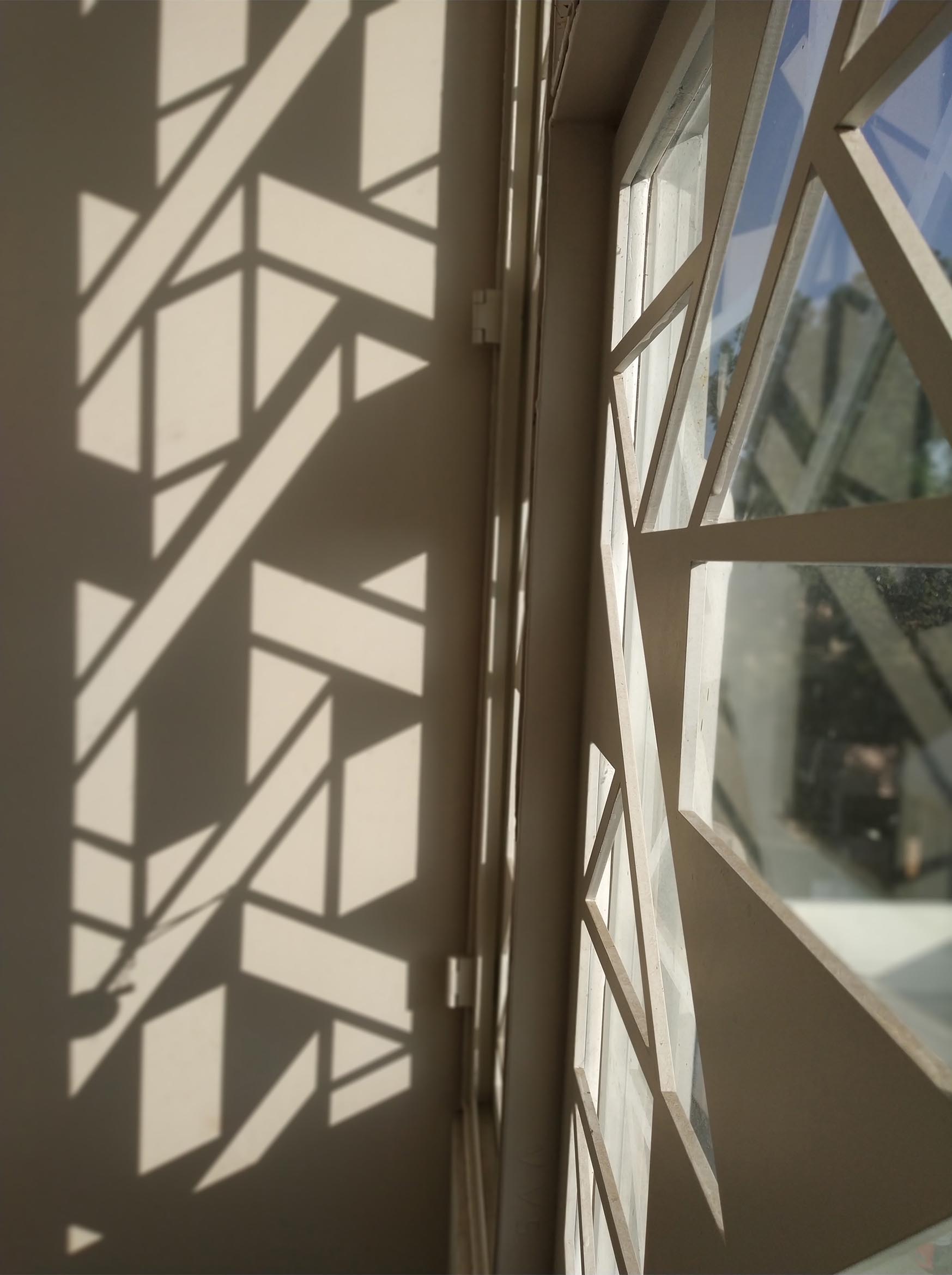 A white window screen with a geometric design casts interesting shadows on the walls and floor.