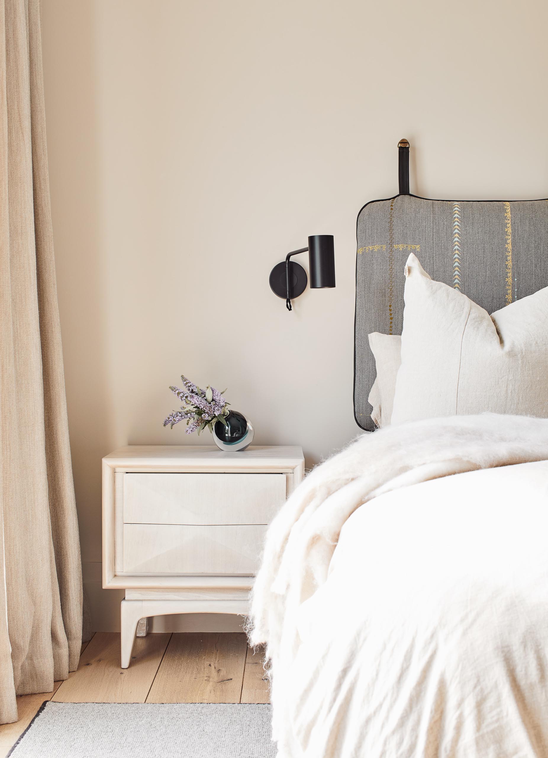 In this guest bedroom, the upholstered headboard hangs from the wall, while minimalist black sconces are positioned above bedside tables.