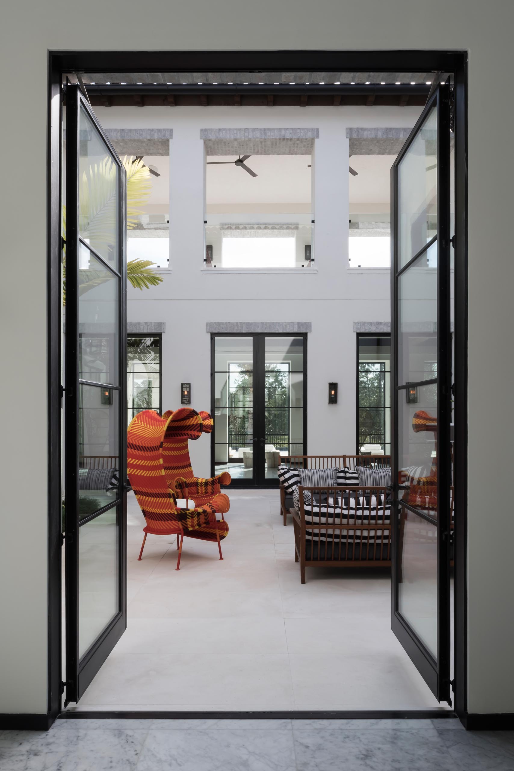 An internal courtyard has a tiled patio with lounges and sculptural chairs, while a garden alongside one wall adds greenery.