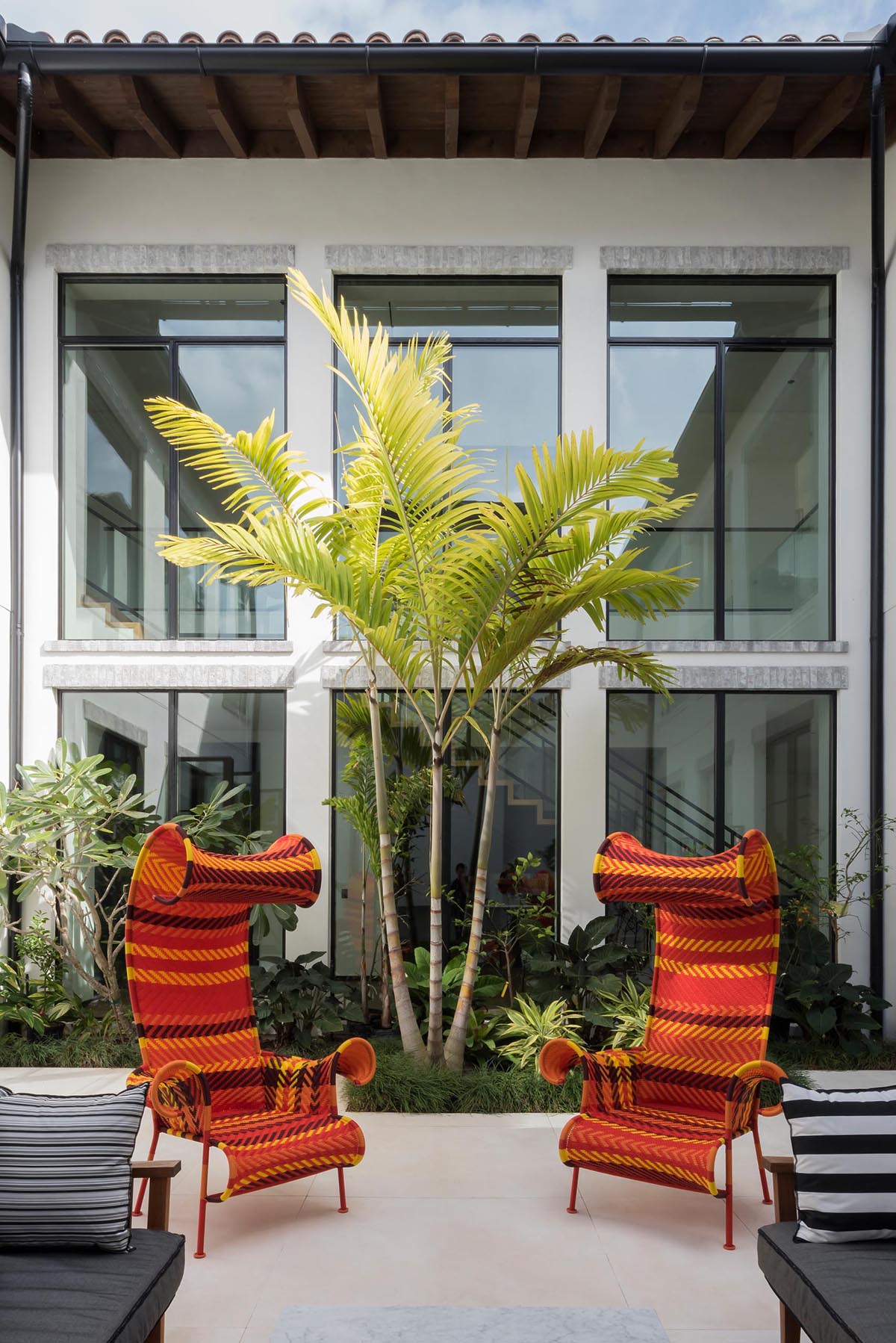 An internal courtyard has a tiled patio with lounges and sculptural chairs, while a garden alongside one wall adds greenery.