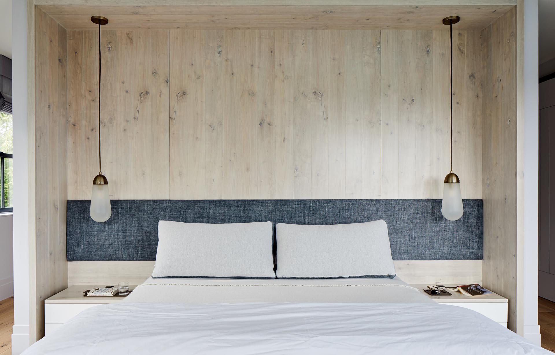 This master bedroom has the bed recessed into an alcove. An upholstered headboard contrasts the wood lined alcove, while pendant lights from Apparatus Studio hang above the bedside tables.