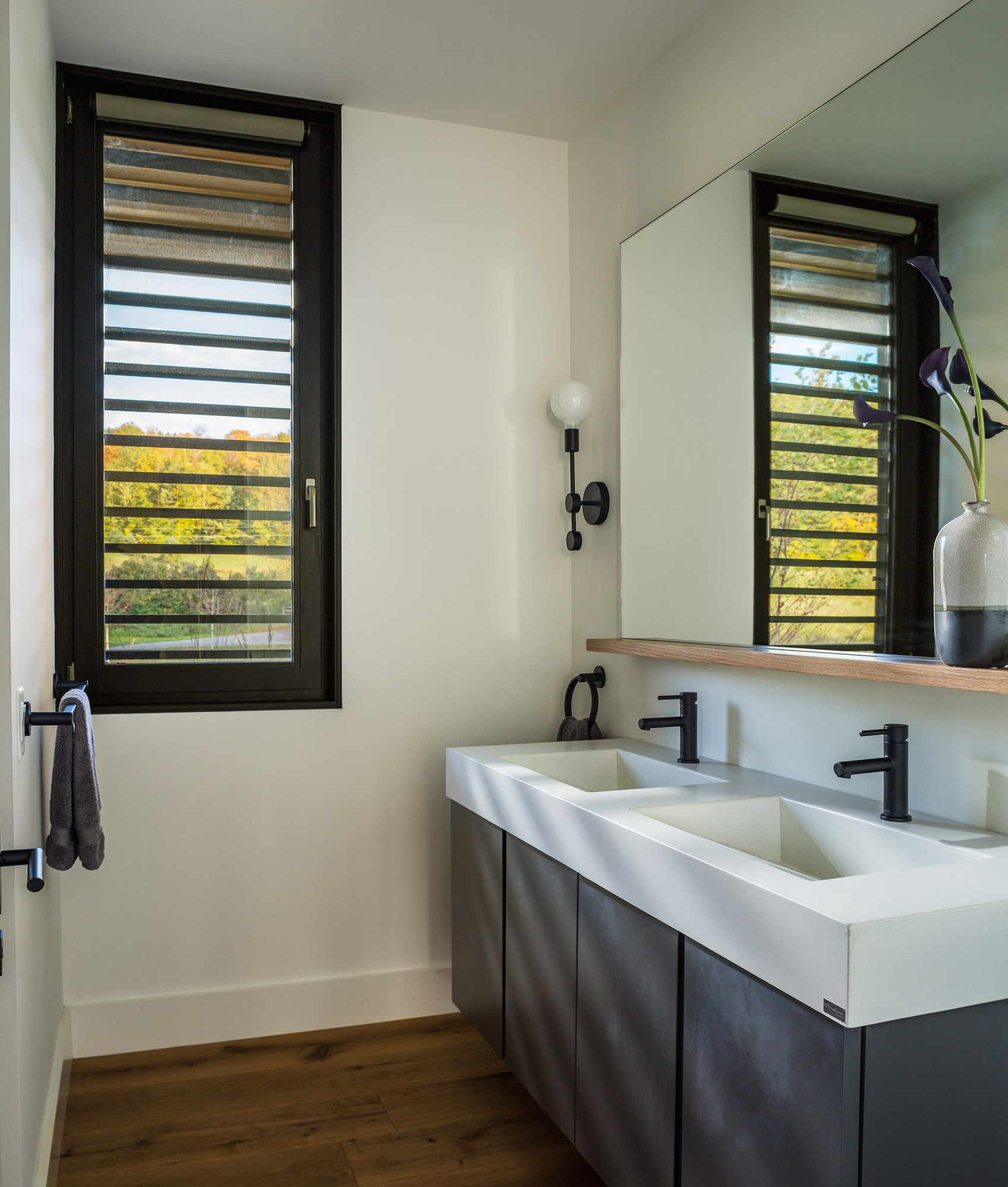 A modern bathroom with a double vanity and a large mirror, matte black light fixtures, and a louver window.