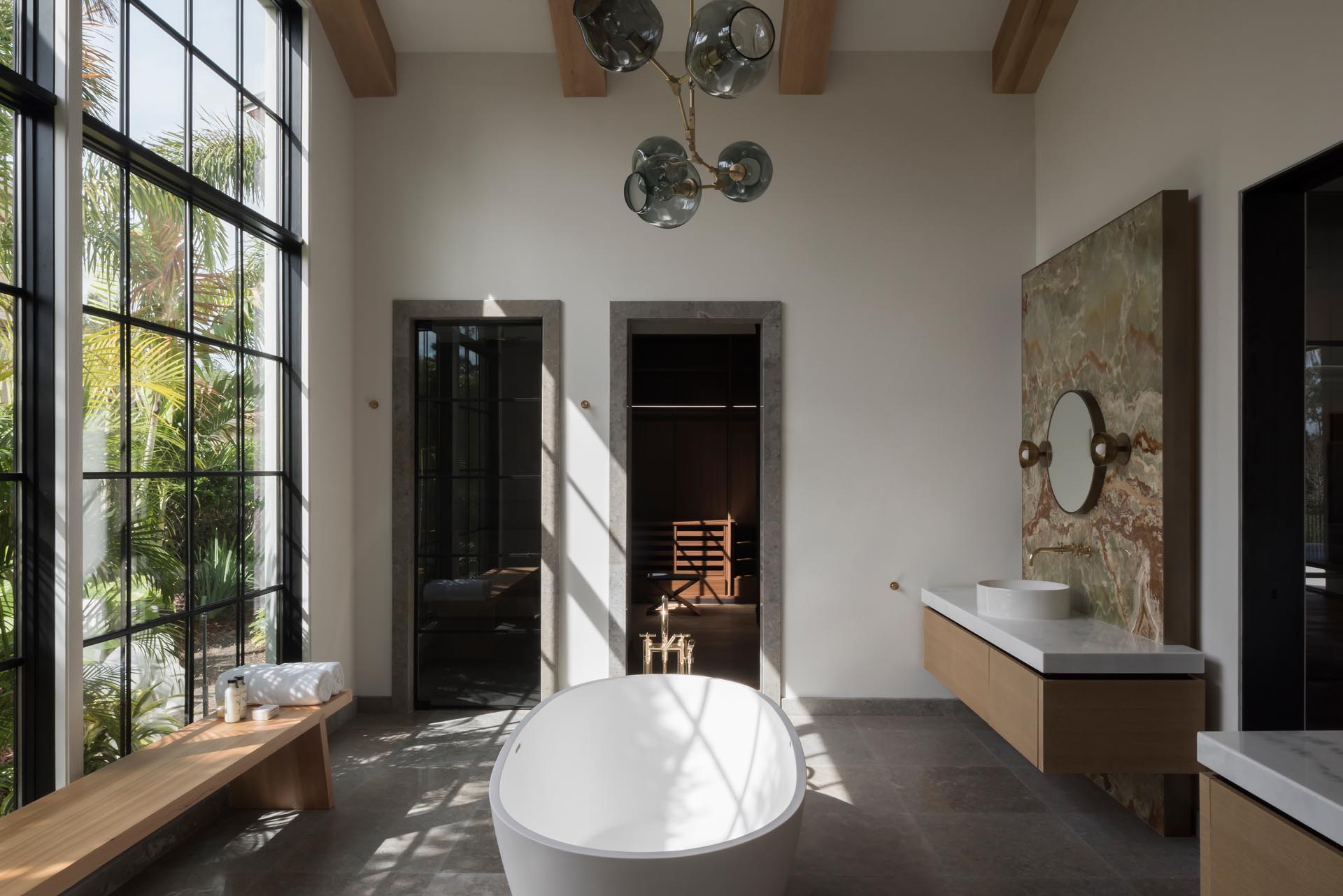 In this modern bathroom, tall windows flood the interior with natural light, while a freestanding bathtub takes center stage.