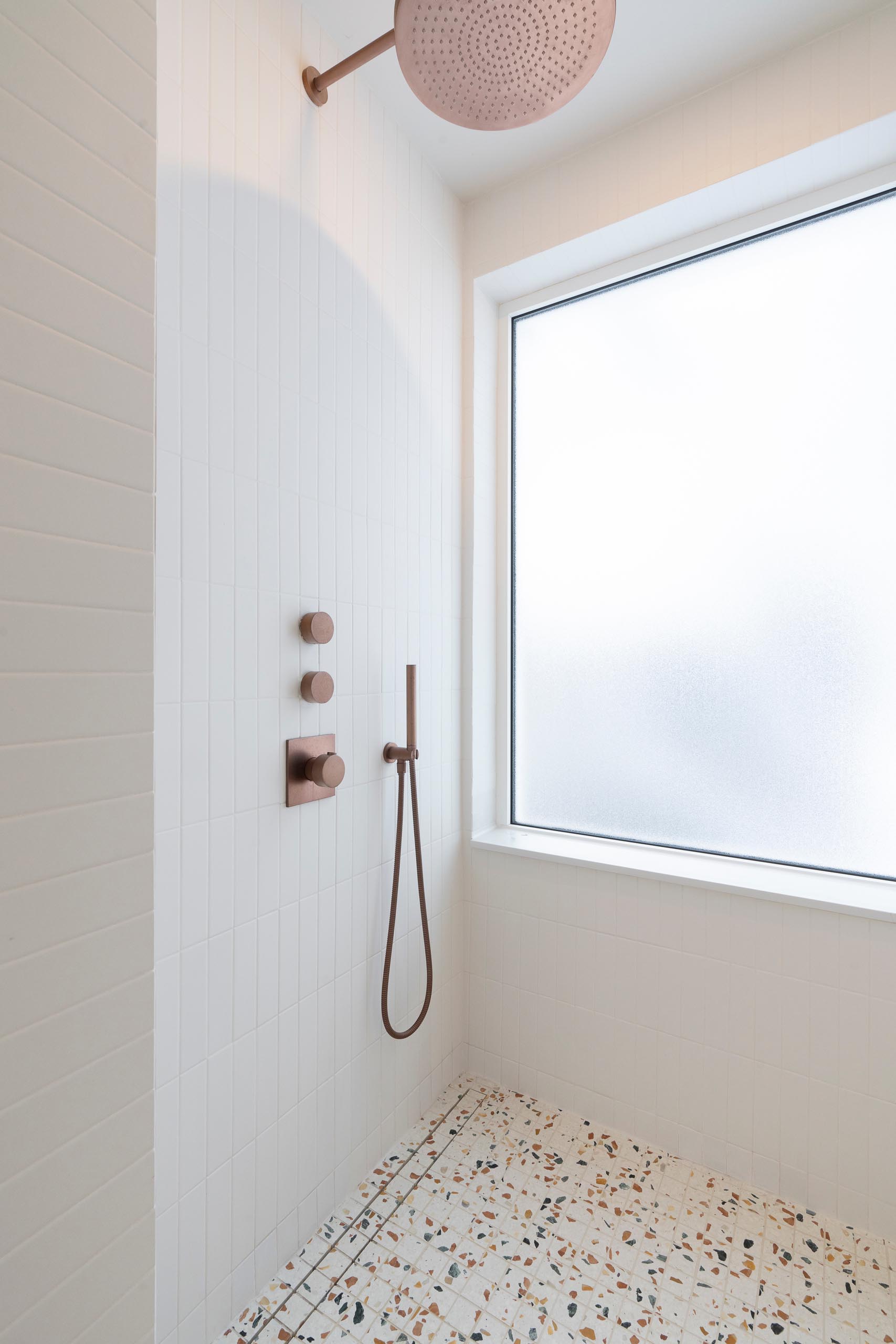 In this modern master bedroom bathroom, the shower features simple white tiles and a colorful terrazzo floor.