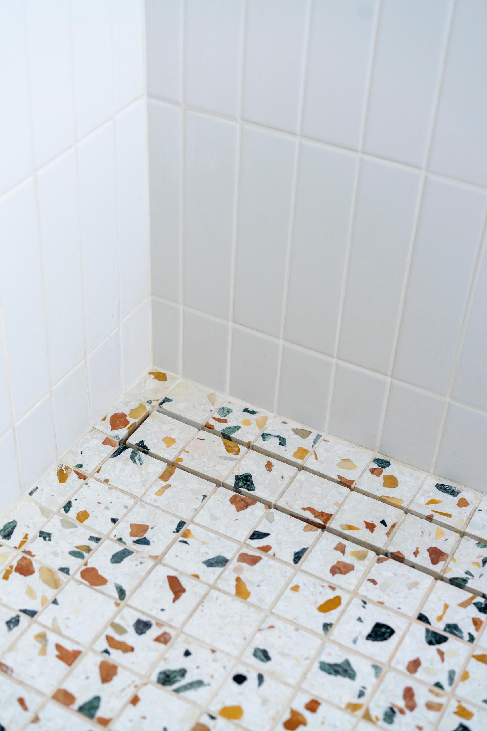 In this modern master bedroom bathroom, the shower features simple white tiles and a colorful terrazzo floor.